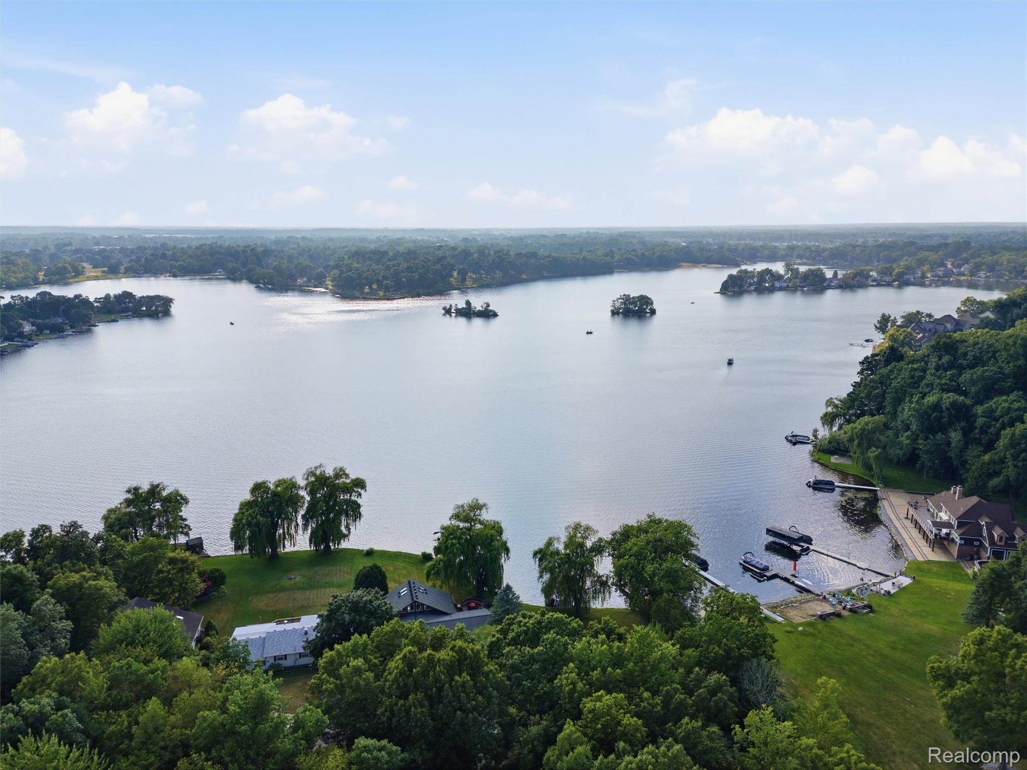 Aerial view of a wooded lakeshore community with homes, docks, and small islands.