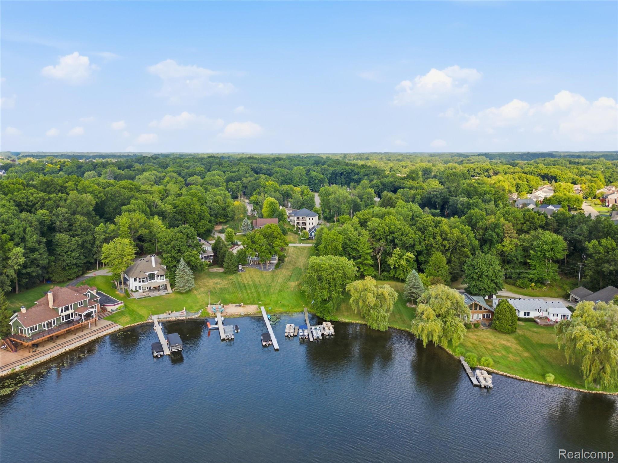 Aerial view of a wooded lakeshore neighborhood with homes, lawns, and several docks.