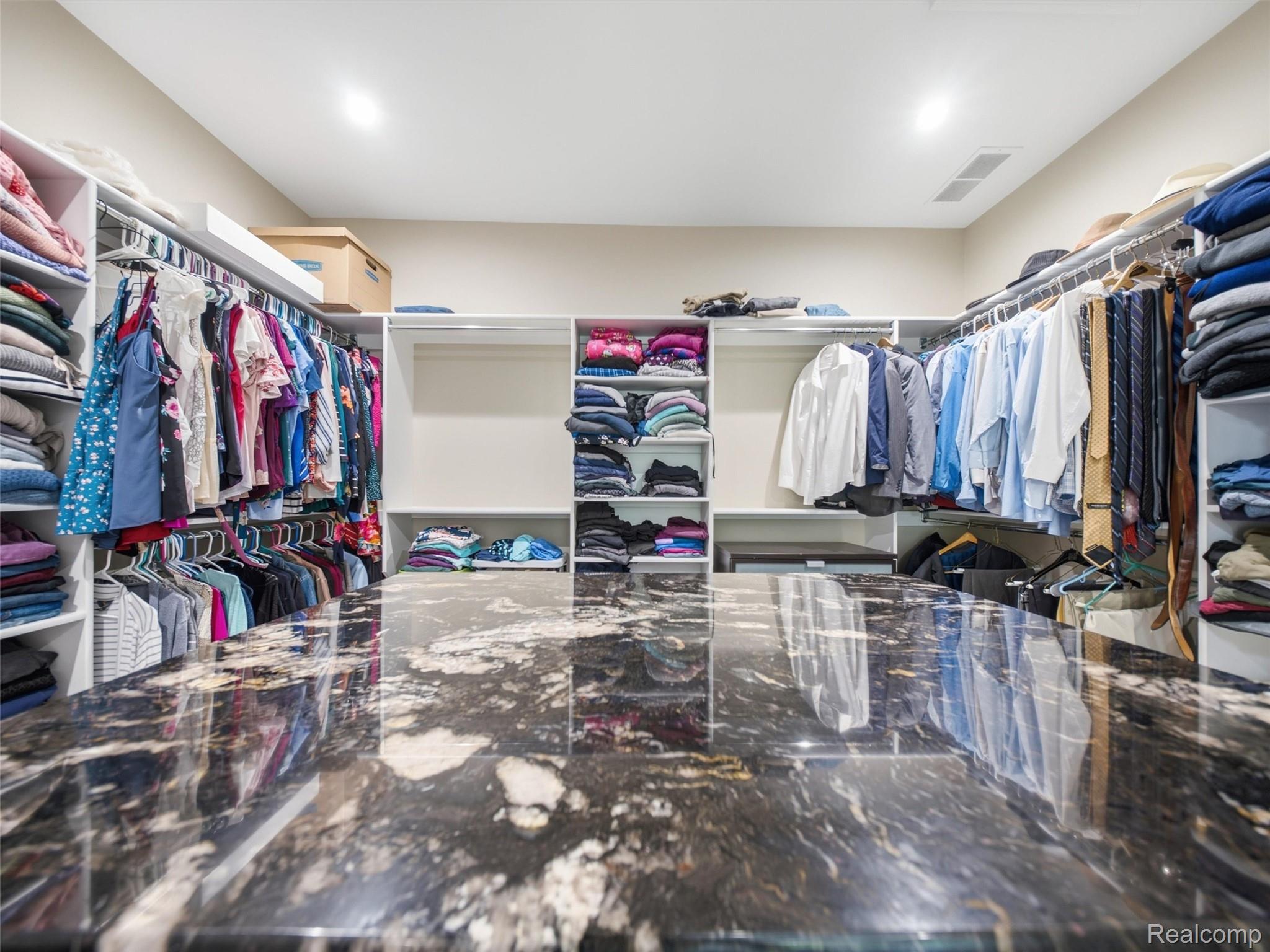 Walk-in closet with built-in clothing shelves and a large stone island.