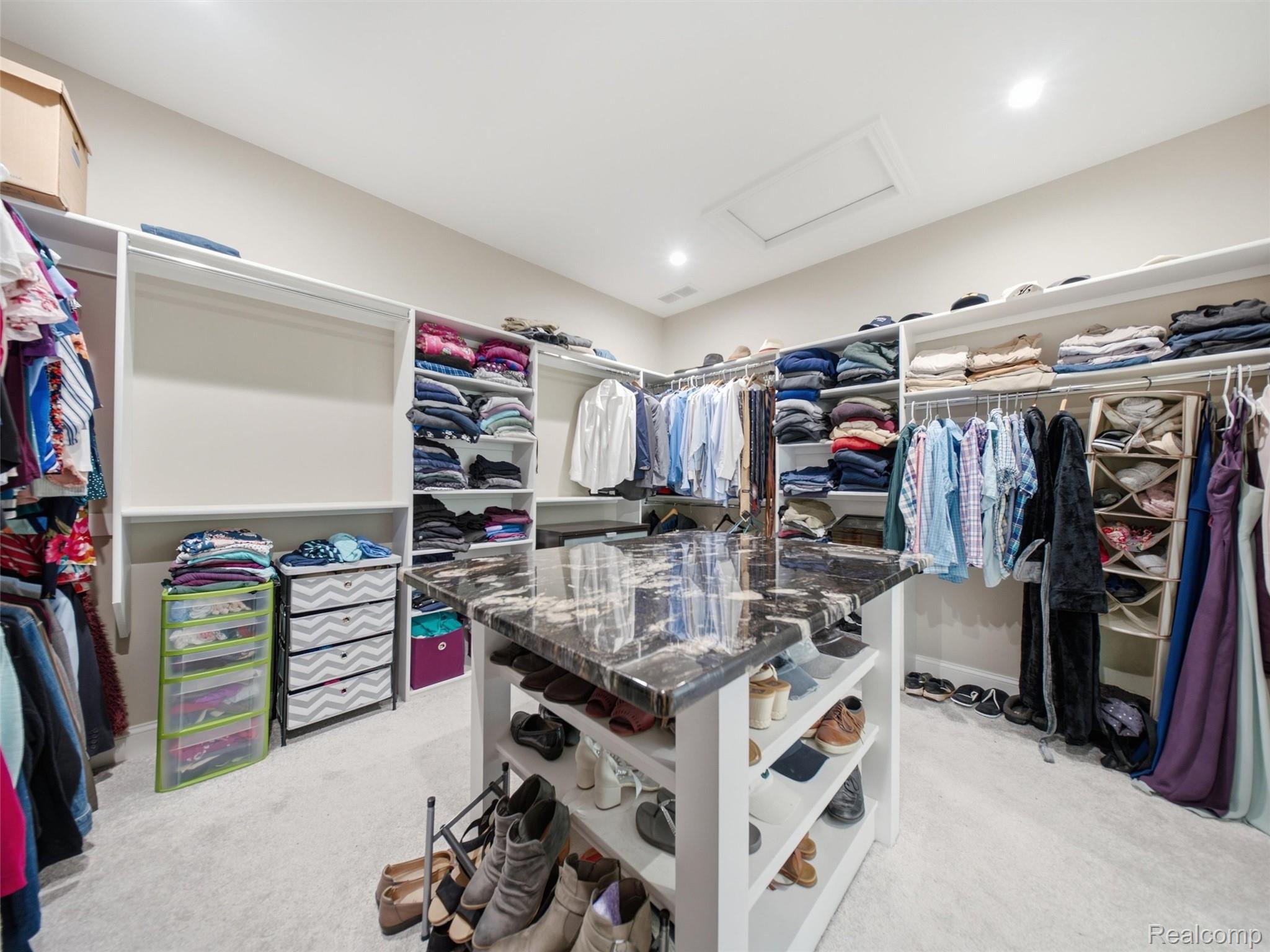 Walk-in closet with extensive clothing storage and a central island with a dark marbled countertop.
