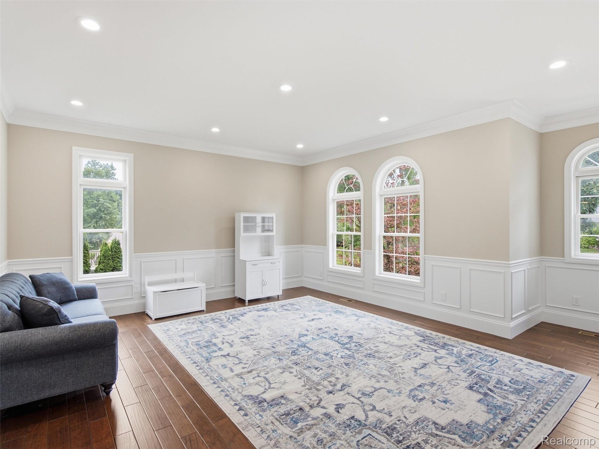Living room with arched windows, white wainscoting, a patterned rug, and dark sofa.