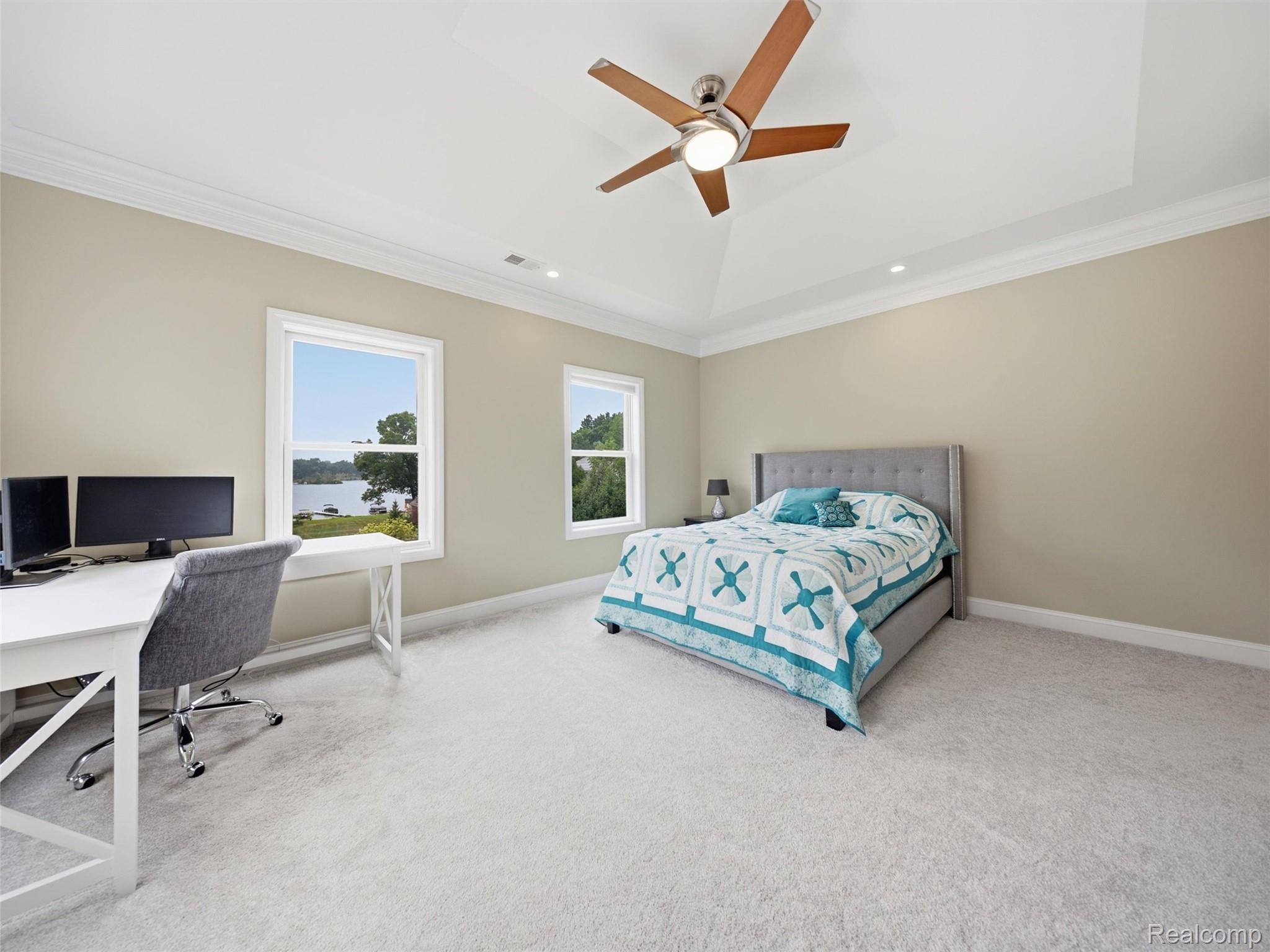 Bedroom with a blue-and-white quilt, desk, ceiling fan, and lake view through the window.