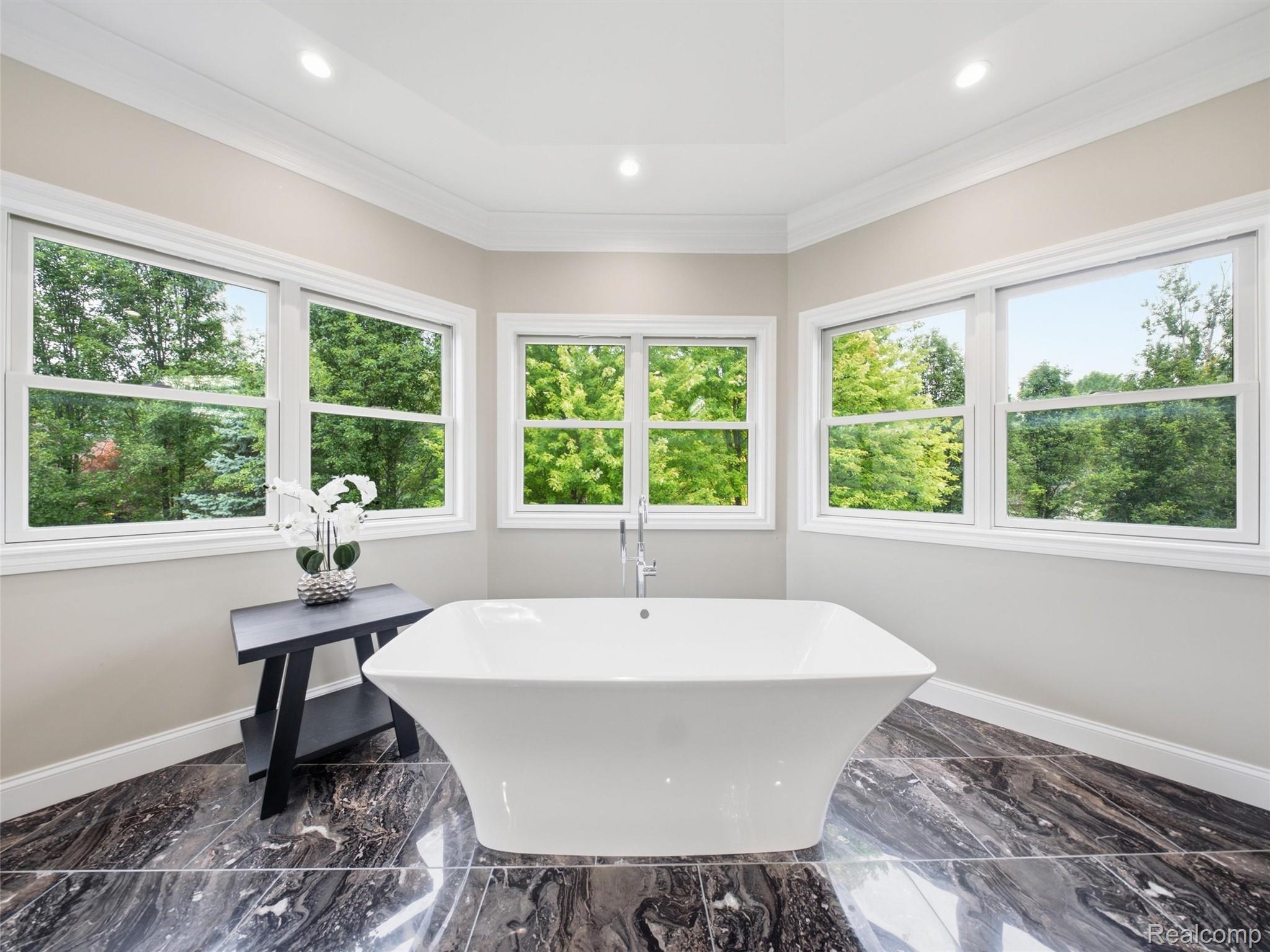 Bathroom with a freestanding soaking tub beneath large windows overlooking trees.