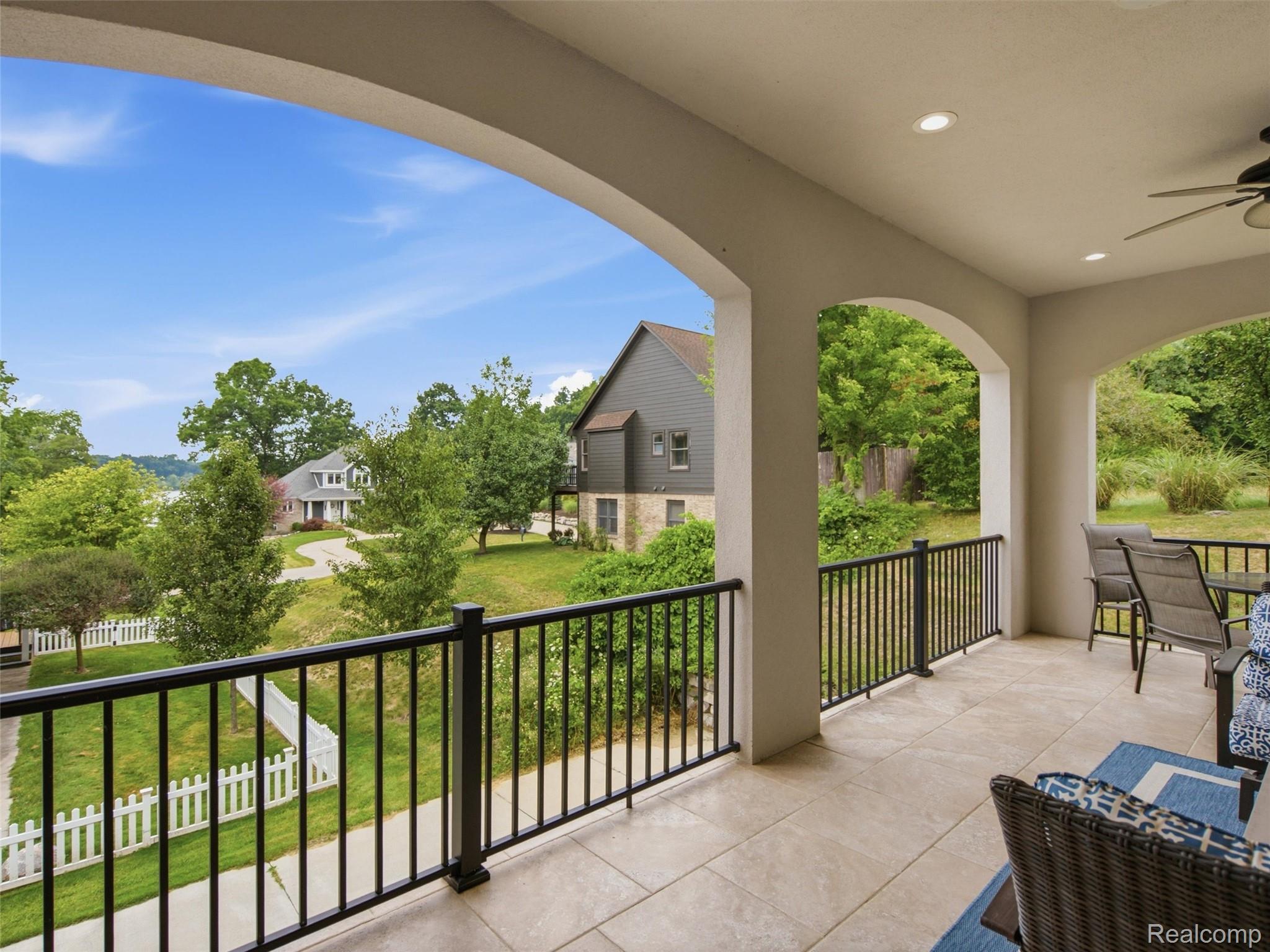 Covered balcony with arched openings and patio seating overlooking leafy yards and neighboring homes.