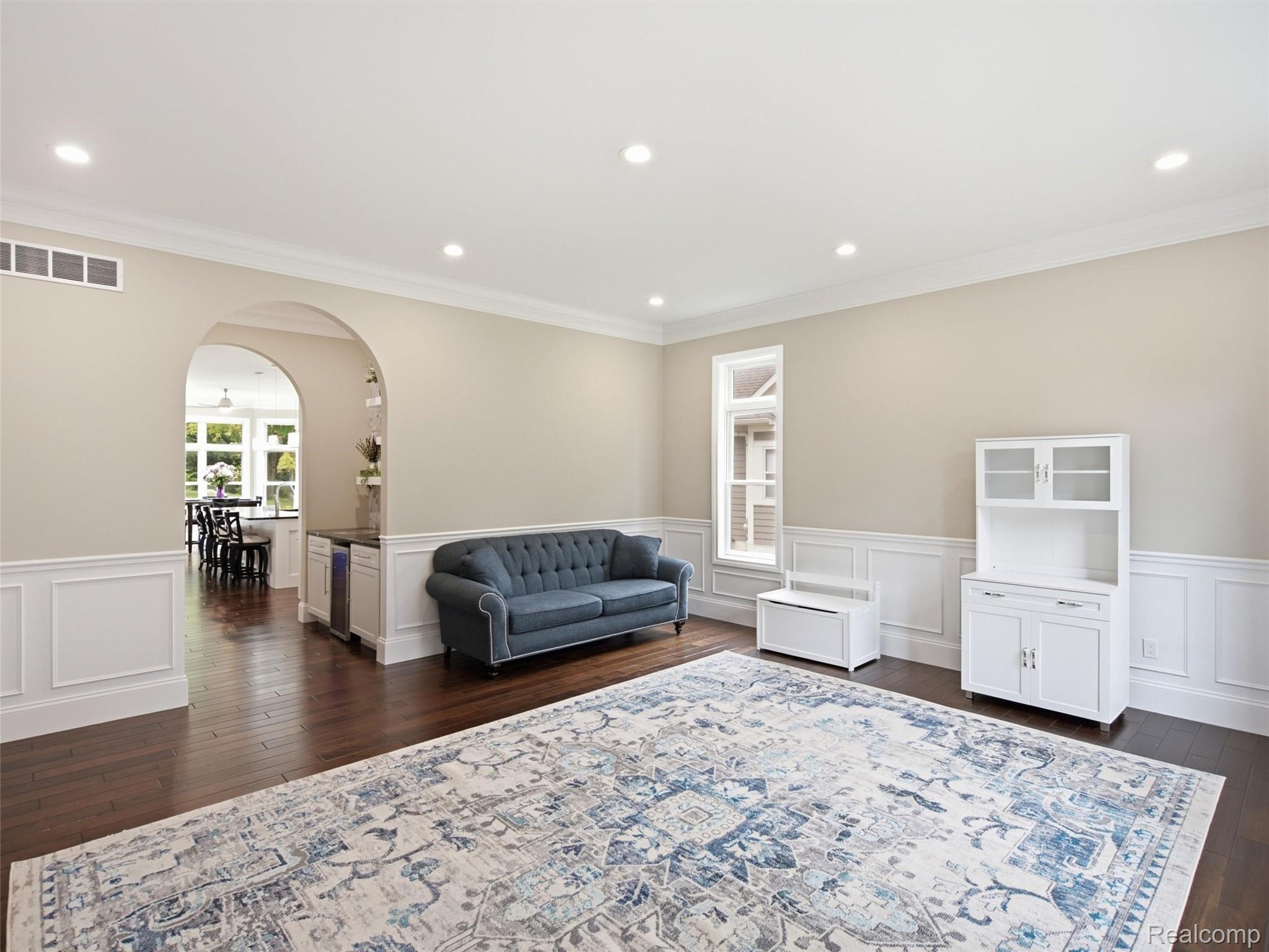 Living room with a blue tufted sofa, patterned rug, and arched opening to the dining area.