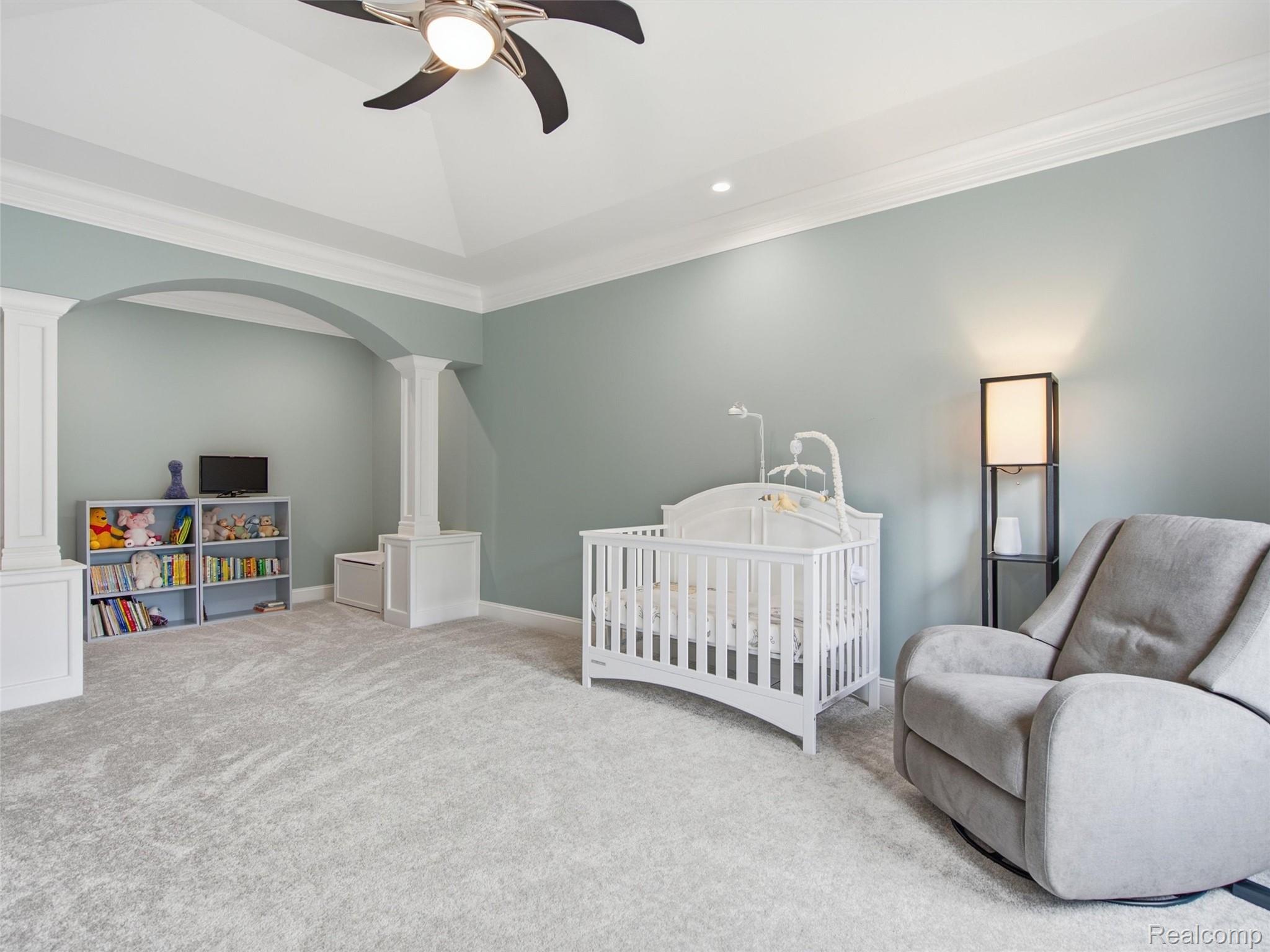 Nursery with a white crib, gray glider, toy shelves, and tray ceiling.