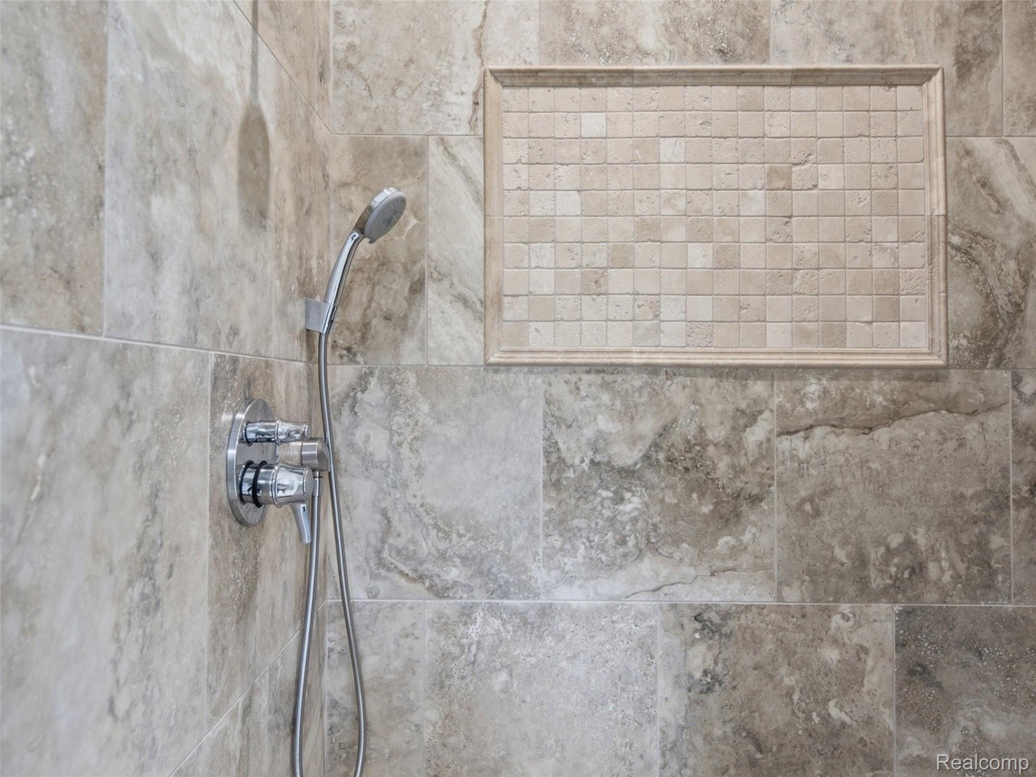 Tiled shower with a recessed square-tile niche and chrome handheld showerhead.
