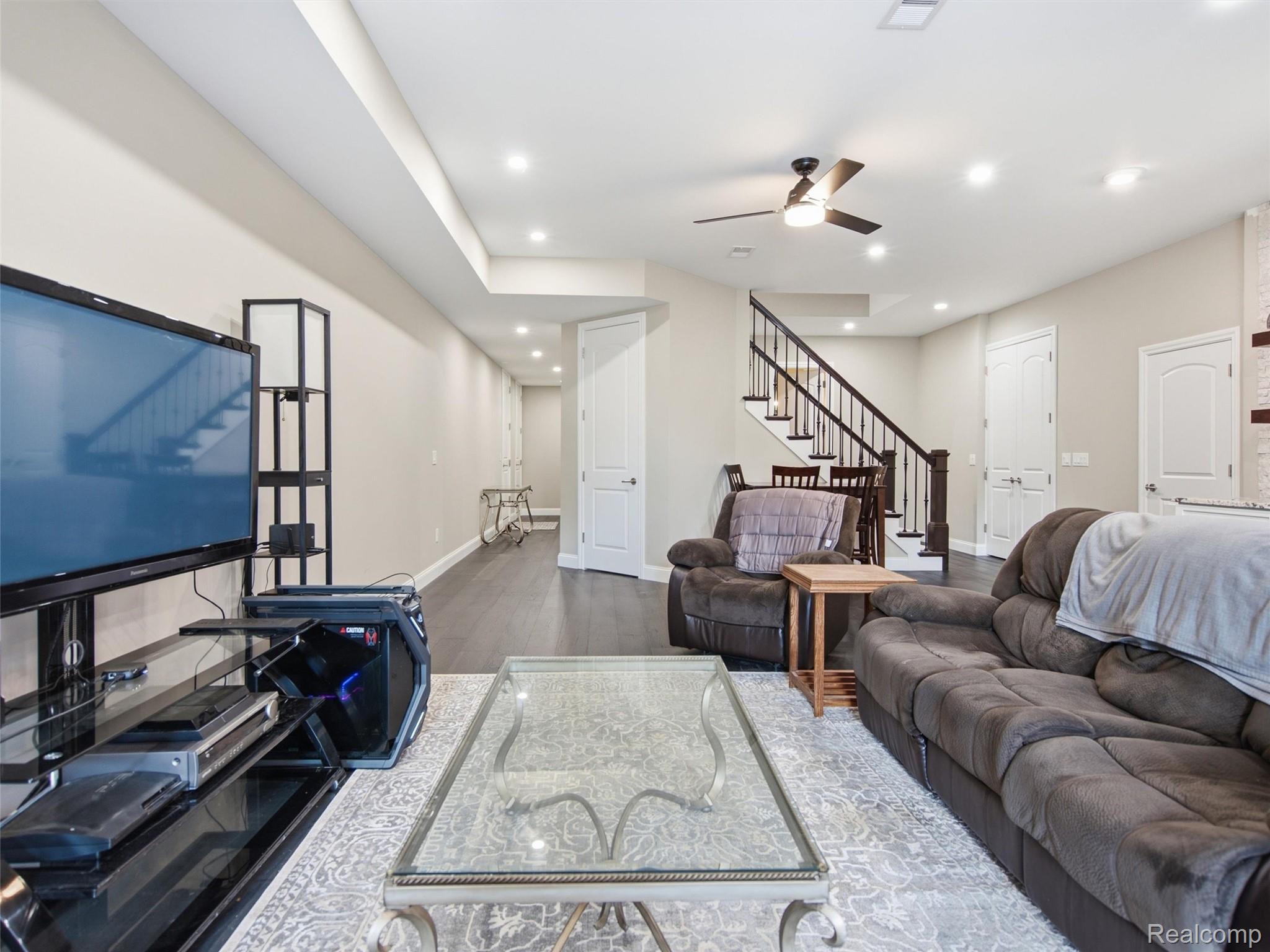 Living room with a glass coffee table, sectional sofa, television, and staircase.