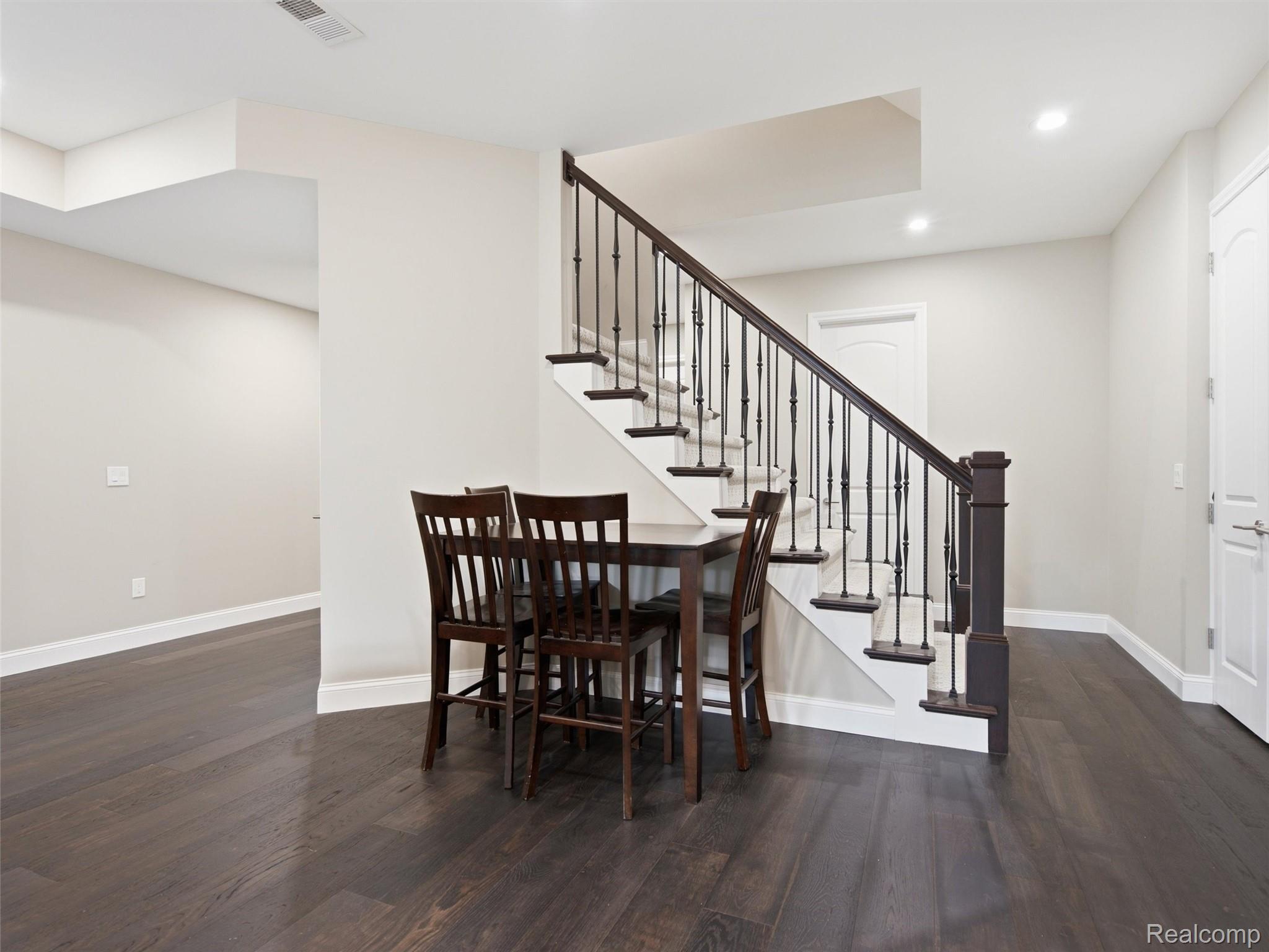 Dining area with dark wood furniture beside a carpeted staircase with dark iron balusters.