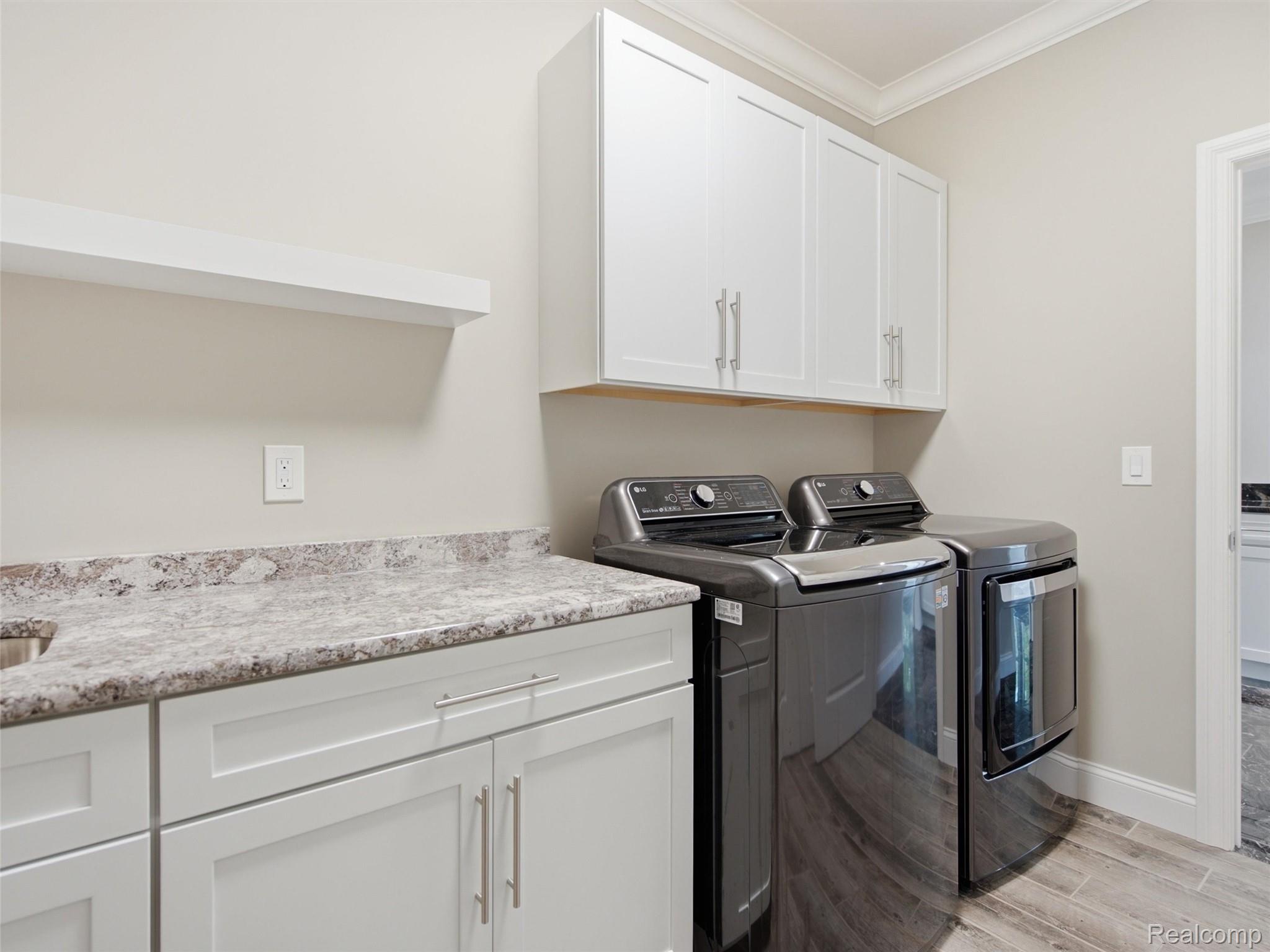 Laundry room with dark washer and dryer beside white cabinetry and a stone-look countertop.