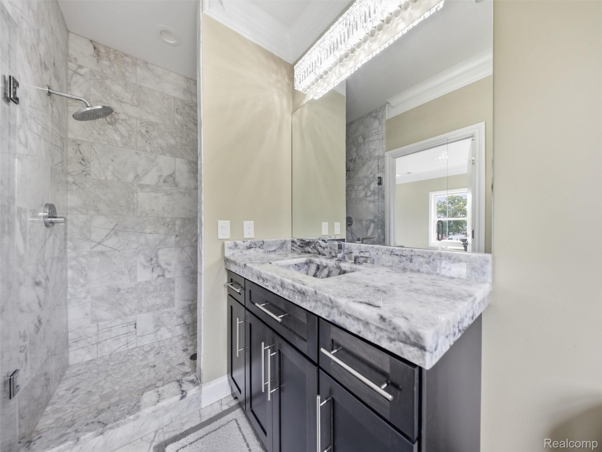 Bathroom with a marble walk-in shower and dark vanity topped with a veined stone counter.