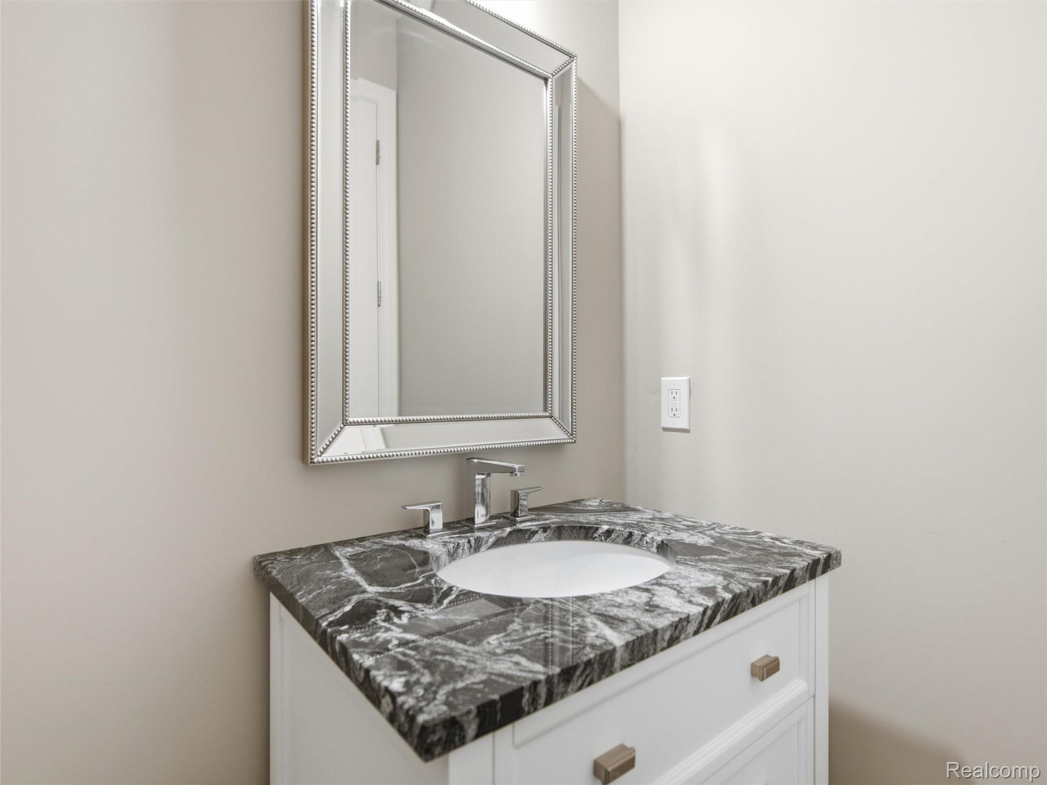 Bathroom vanity with a veined stone countertop, undermount sink, chrome faucet, and framed mirror.