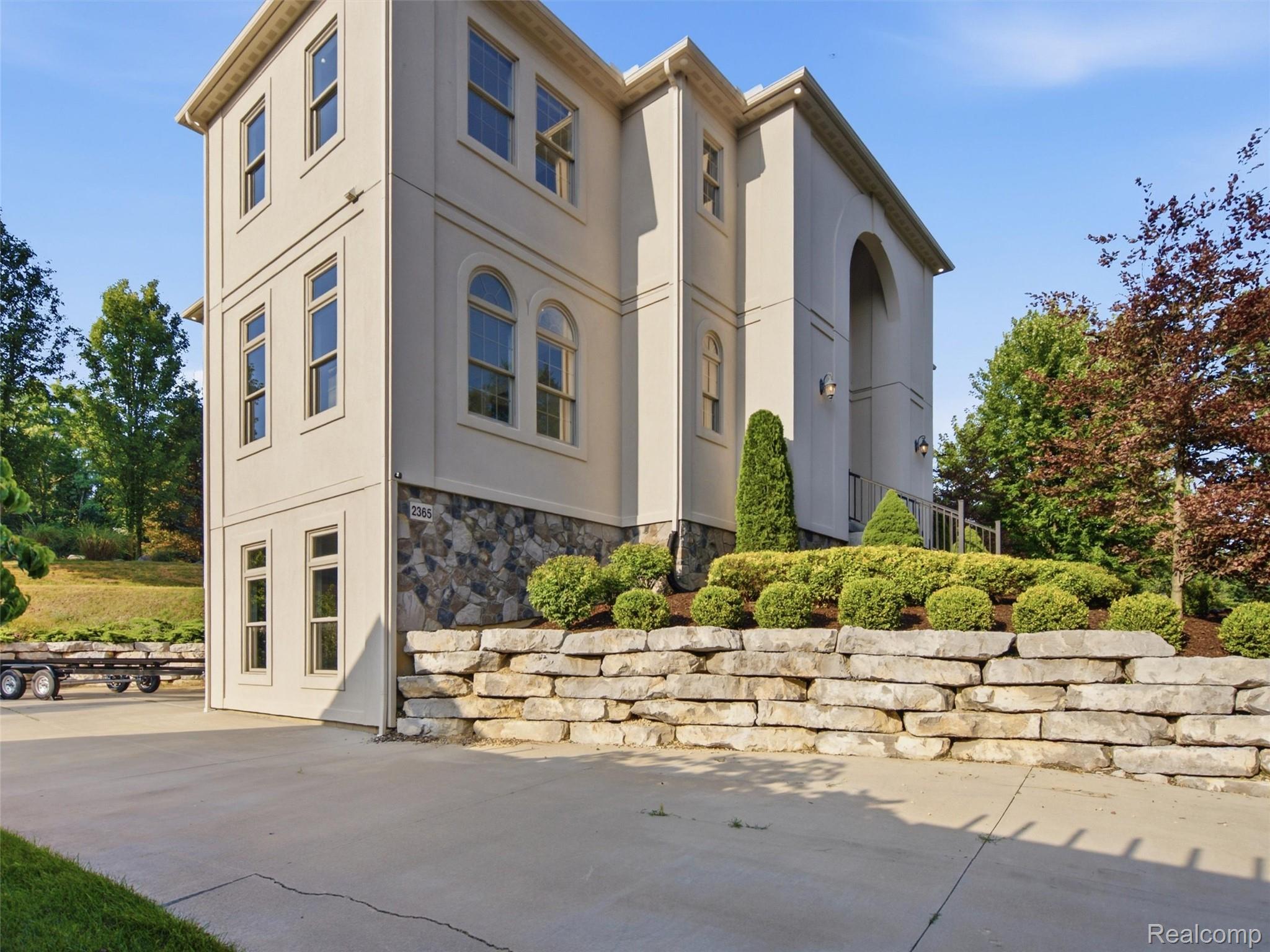 Tall cream-colored house with stone lower level, arched entry, and landscaped retaining wall.