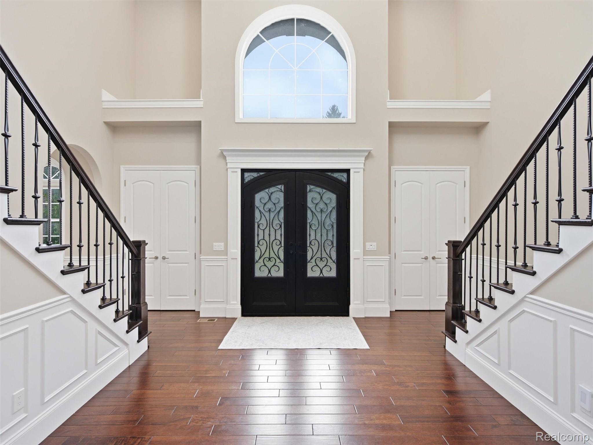Two-story foyer with twin staircases, black glass-paneled entry doors, and a large arched window.