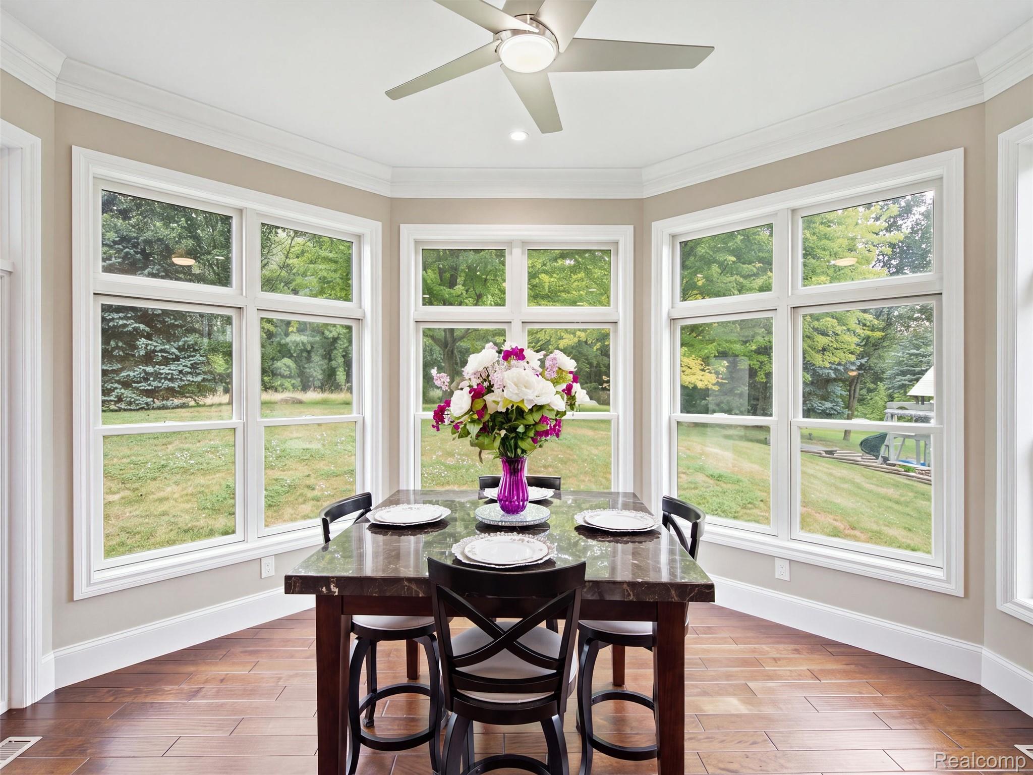 Dining nook with a dark wood table, flower arrangement, and large bay windows overlooking a green yard.