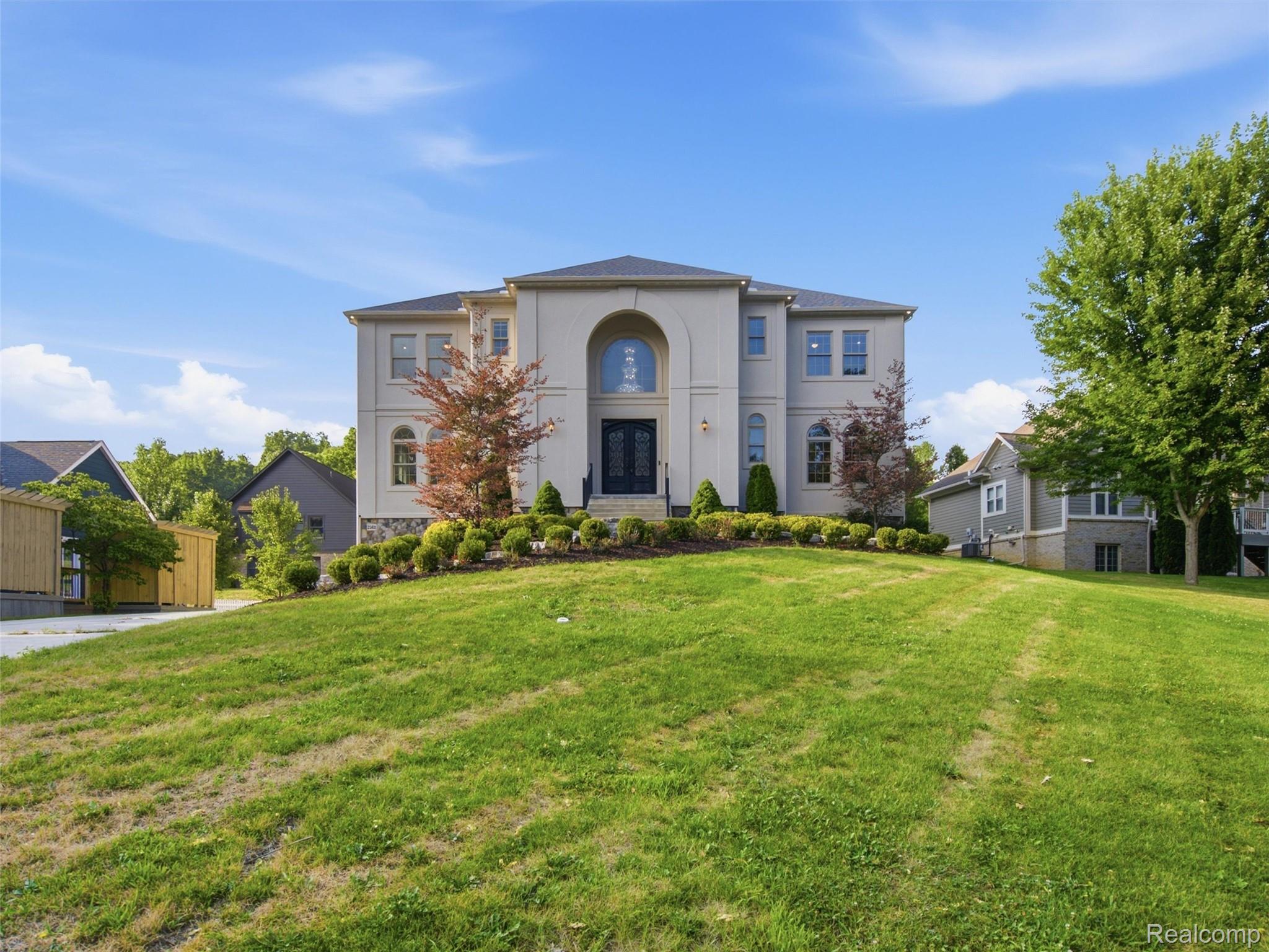 Two-story home with an arched entry, landscaped shrubs, and a broad sloping front lawn.