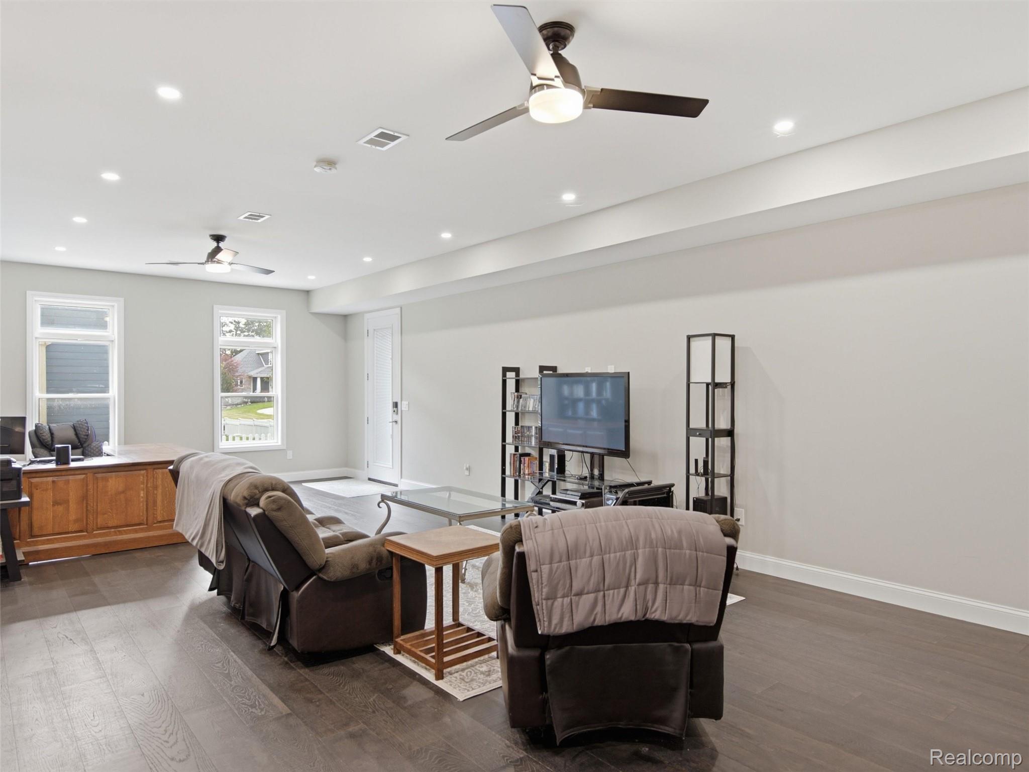 Furnished living room with a TV, two ceiling fans, and dark wood-look flooring.