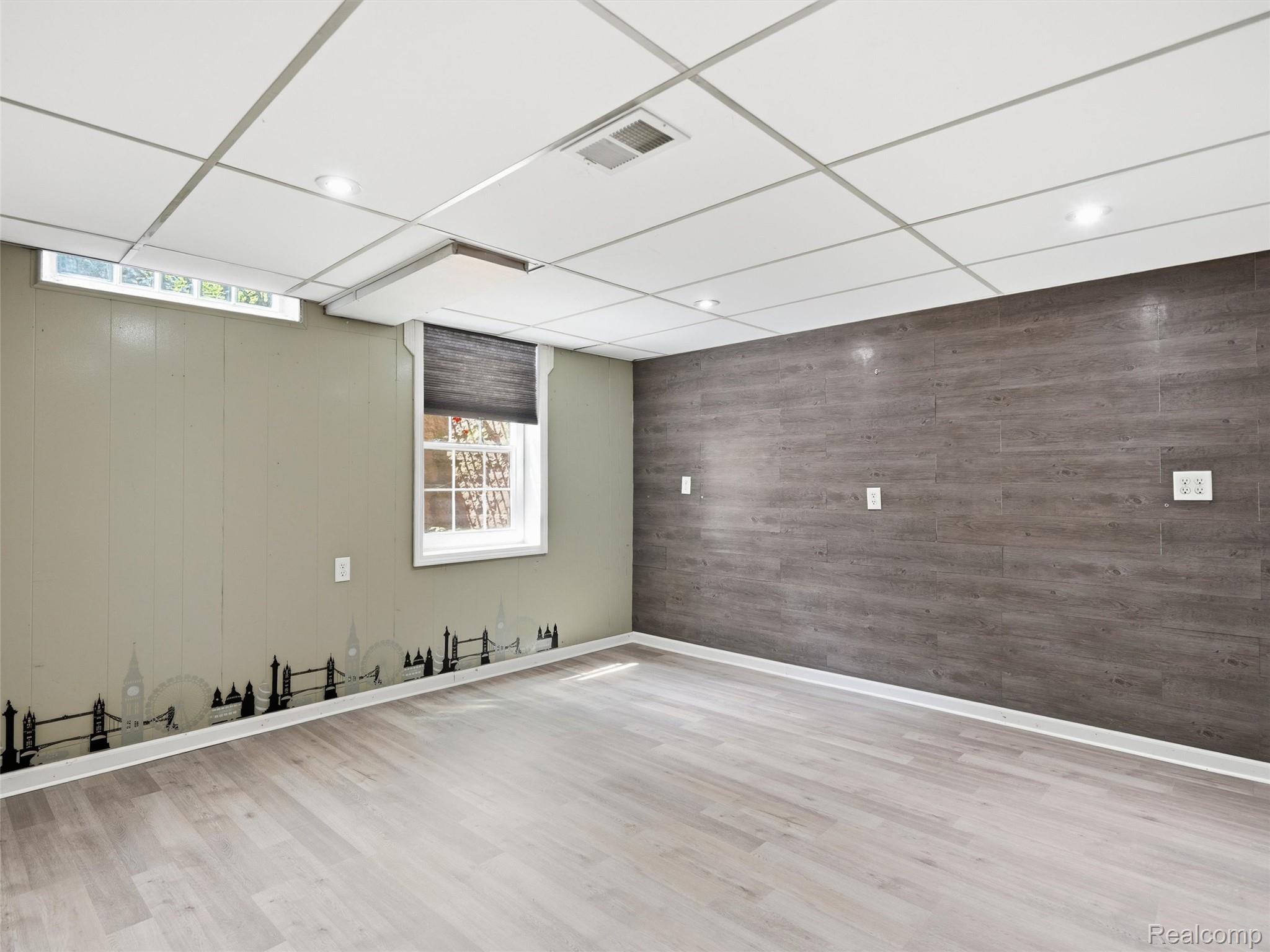 Empty finished room with gray accent wall, wood-look floors, and a London skyline wall border.