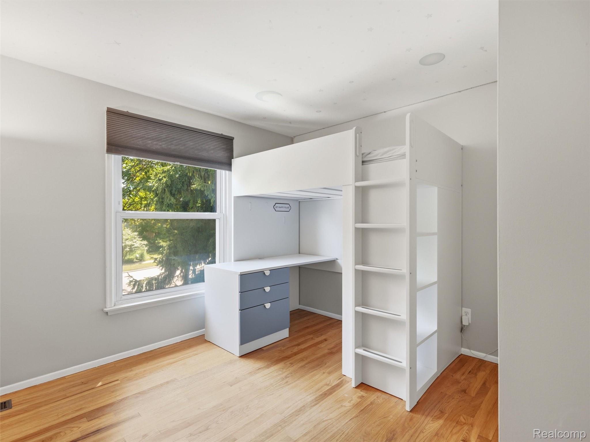 Bedroom with a white loft bed and built-in desk beside a large window.