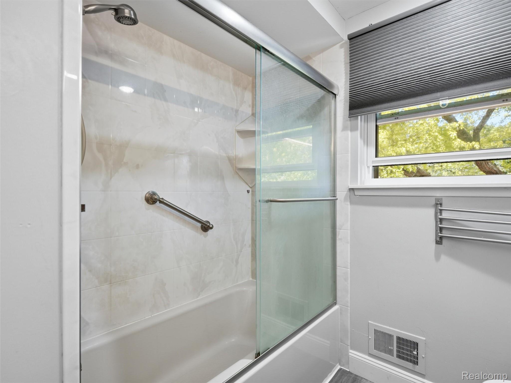 Bathroom with tiled tub-shower, sliding glass doors, a grab bar, and a window.