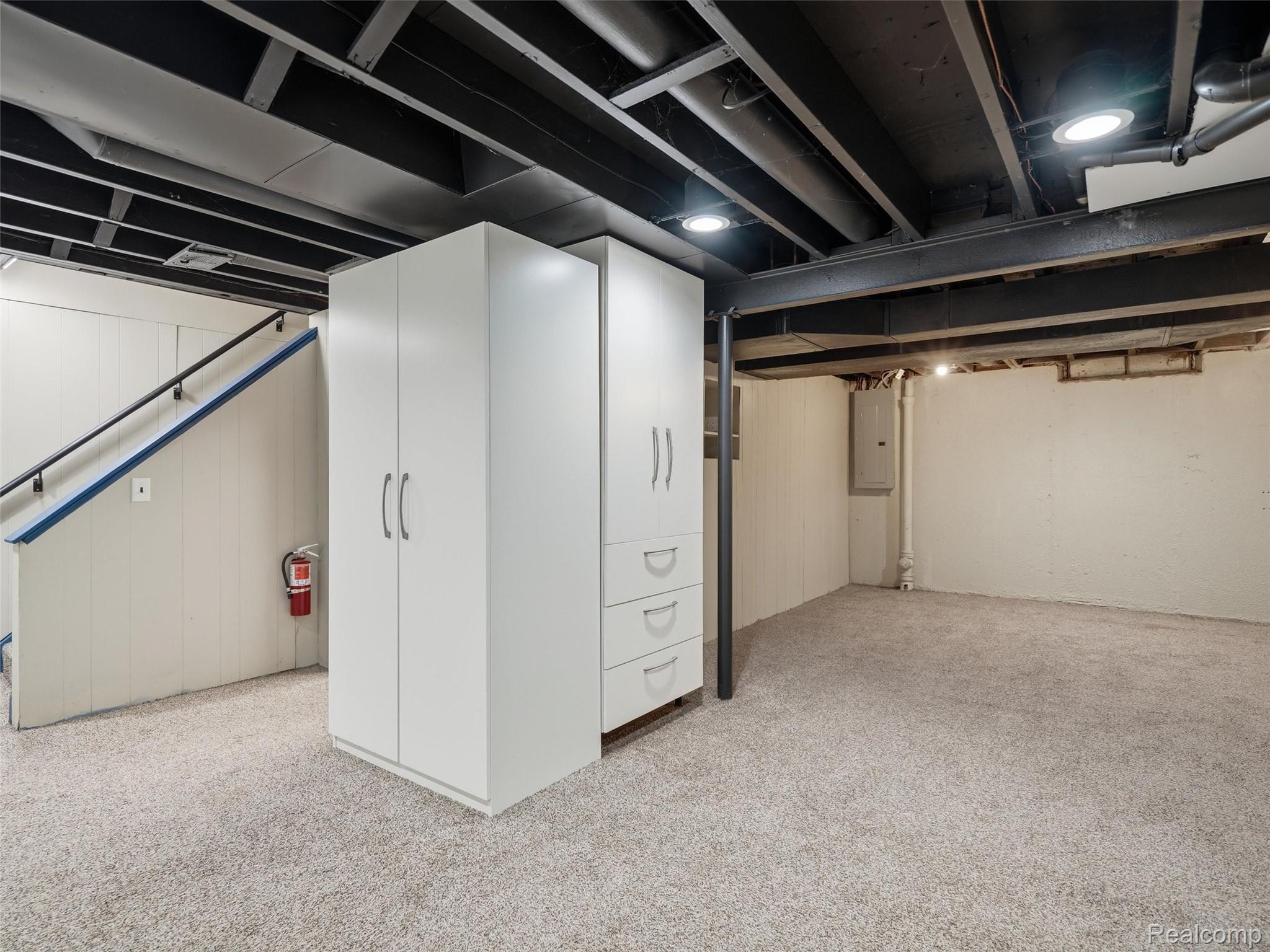 Basement with white storage cabinets, carpeted floor, and exposed ceiling beams.