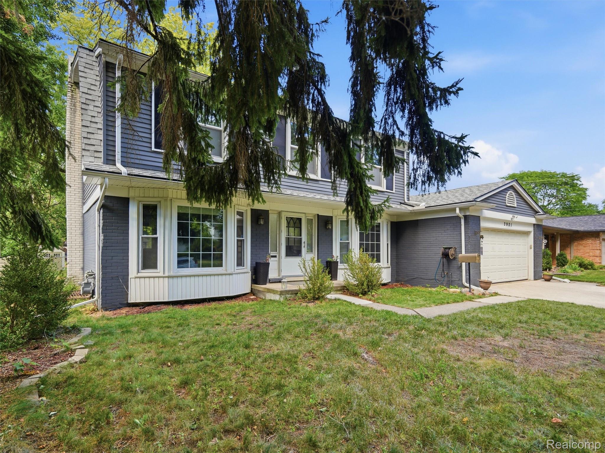 Two-story gray house with white trim, an attached garage, and evergreen branches overhead.