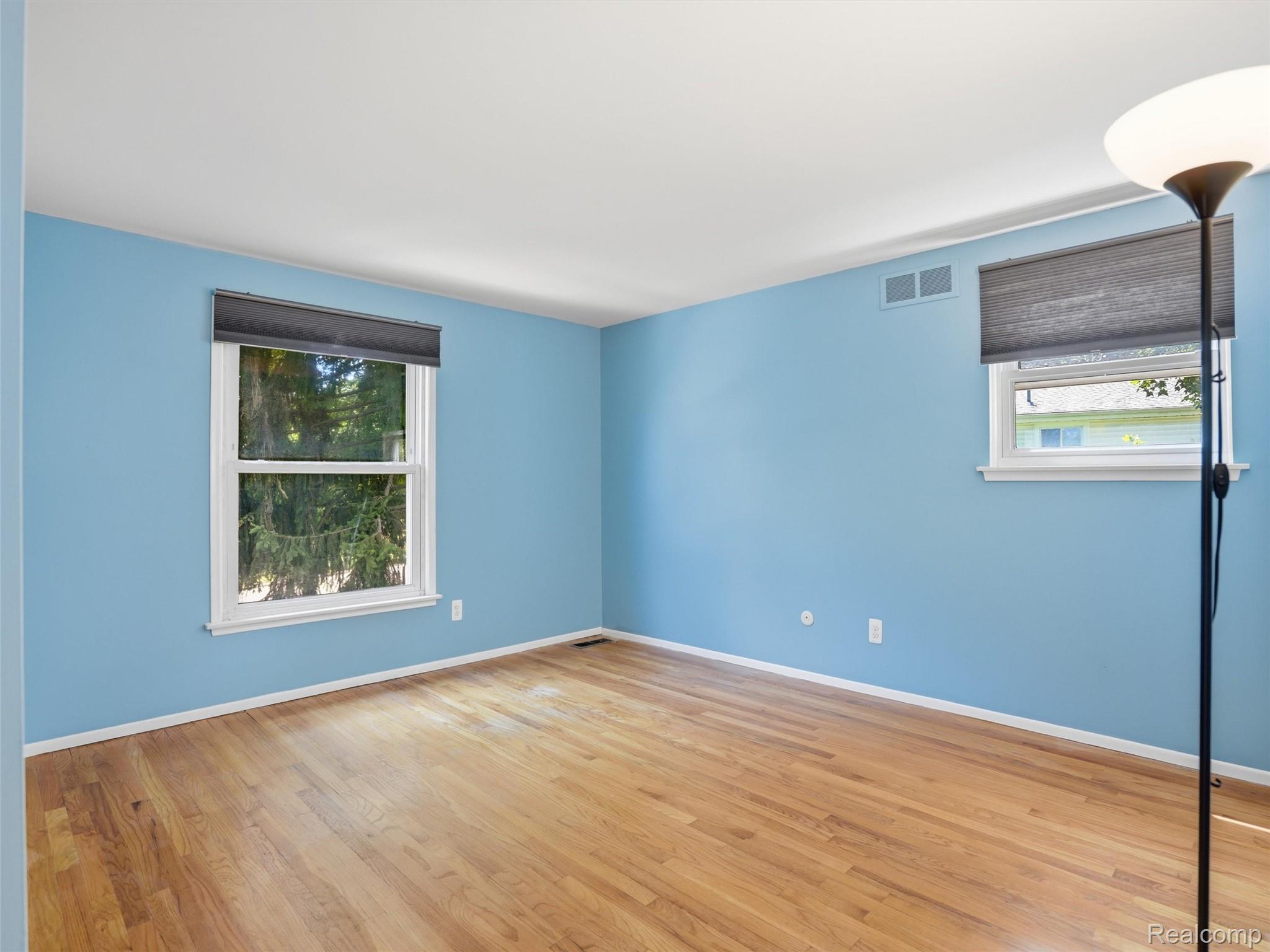 Empty blue room with hardwood floors, two windows, and a floor lamp.
