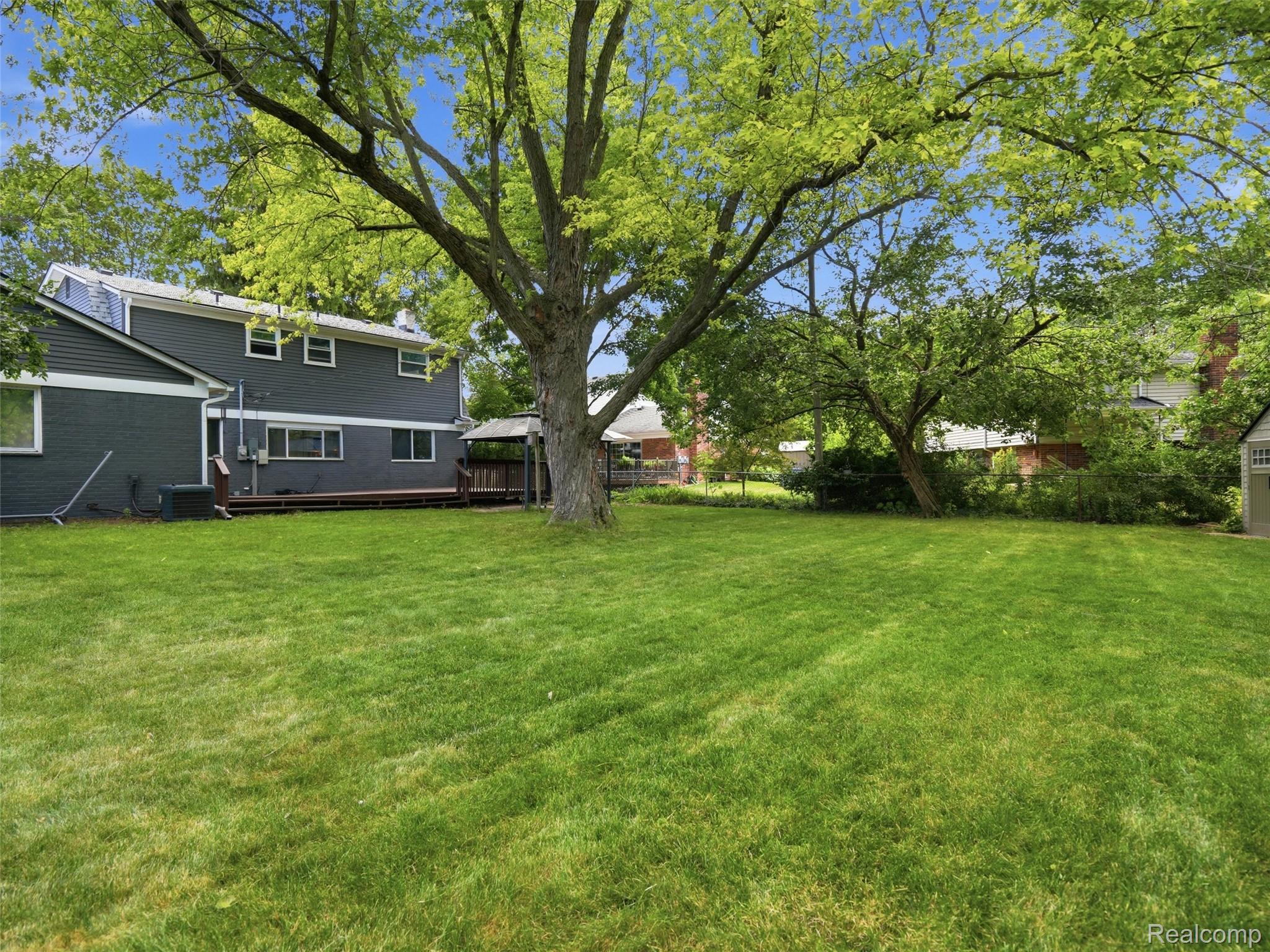 Backyard with a broad lawn, mature shade trees, and a wooden deck behind a dark-sided home.