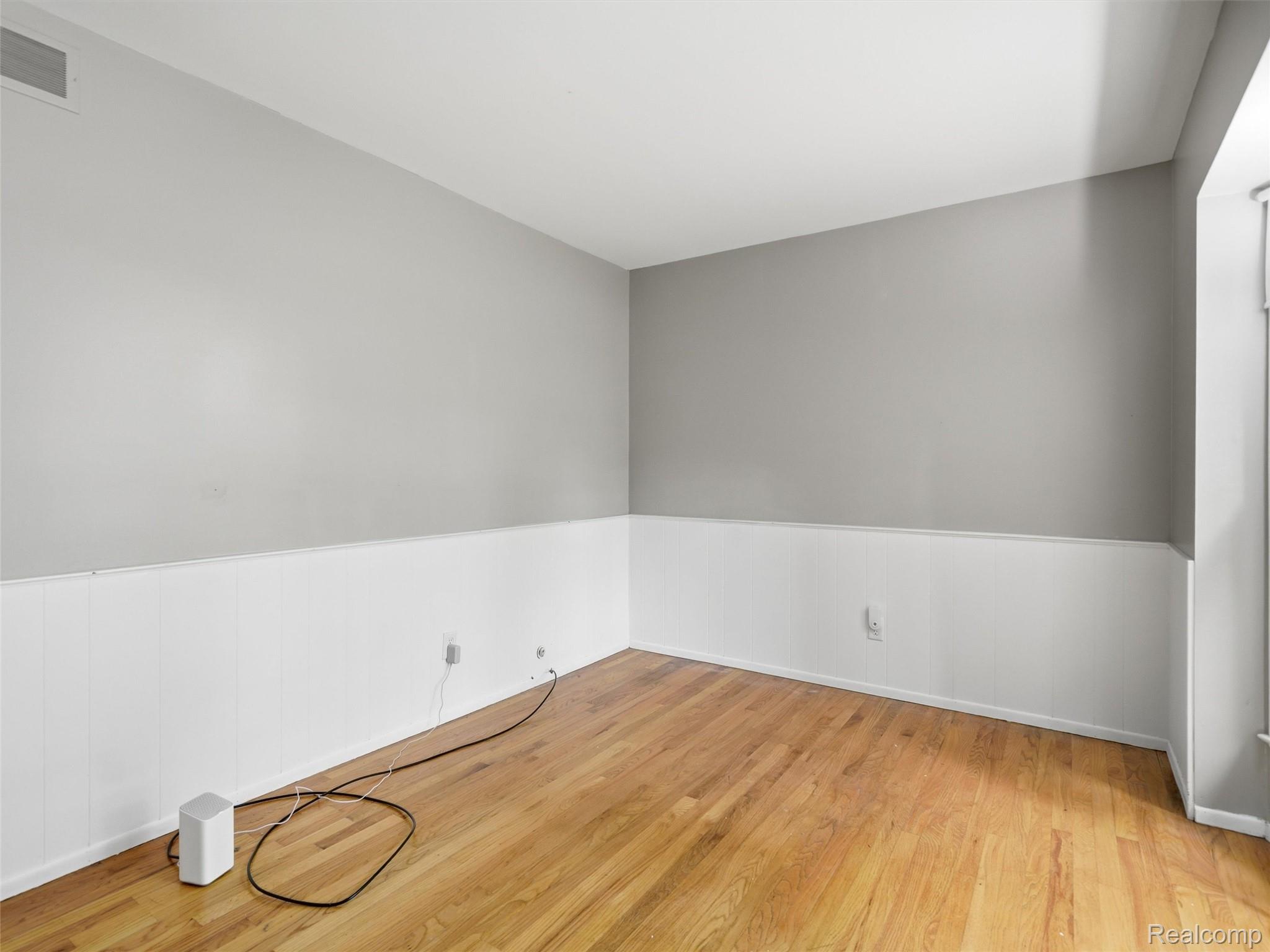 Empty room with hardwood floors, white wainscoting, gray walls, and a sloped ceiling.