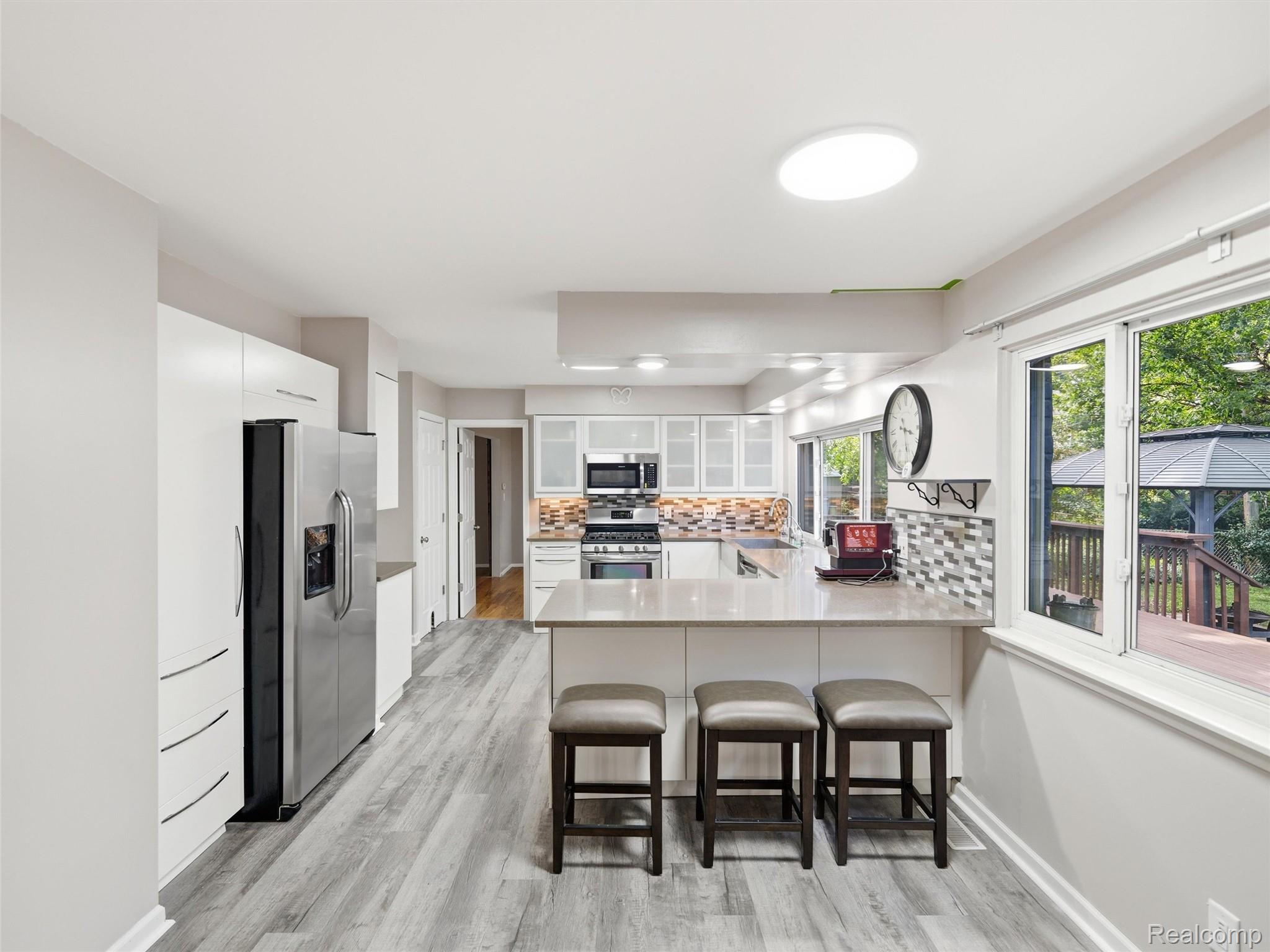 Bright kitchen with white cabinets, stainless appliances, and an island with three stools.