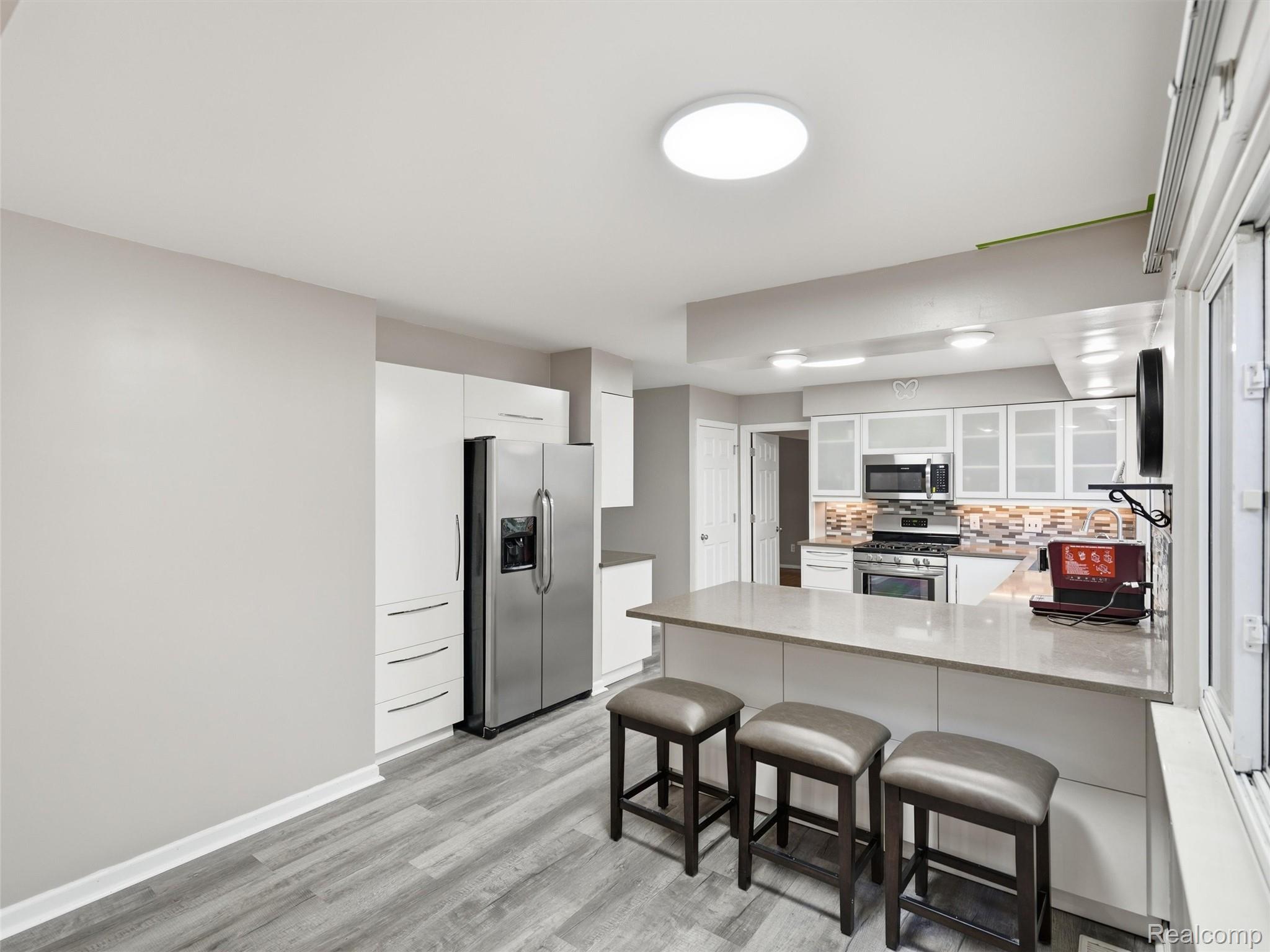 Modern kitchen with white cabinetry, stainless steel appliances, and a large island with three stools.