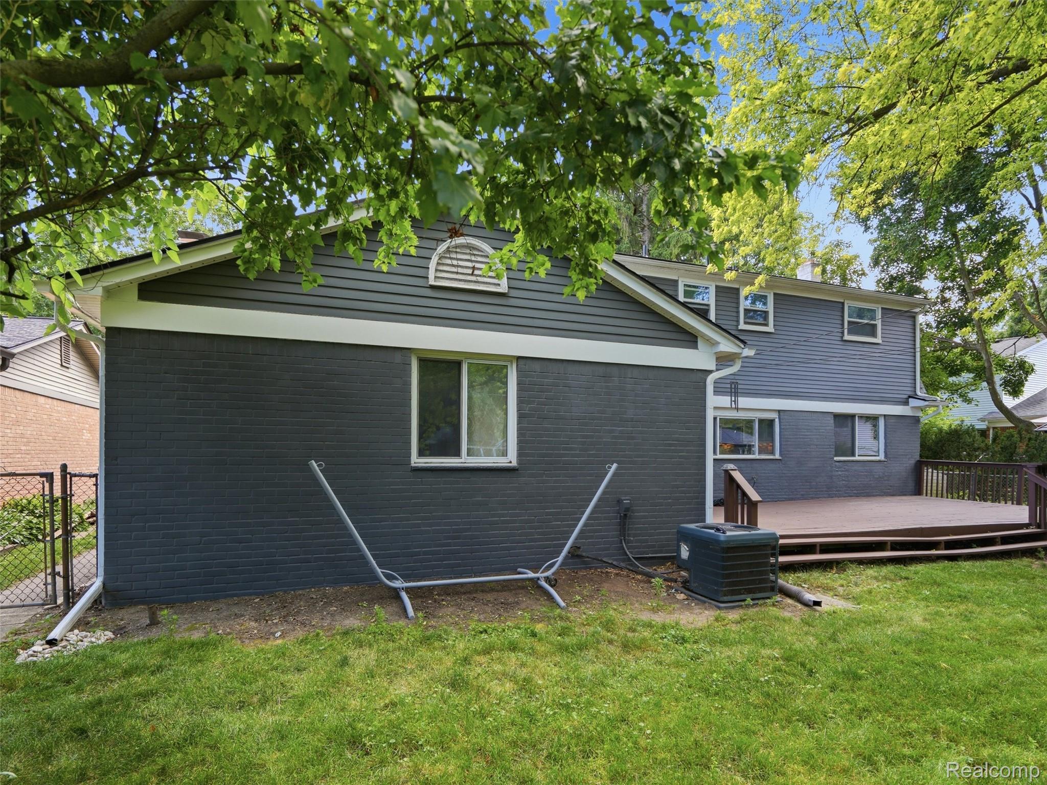 Gray two-story house with a raised wooden deck, viewed from the backyard.