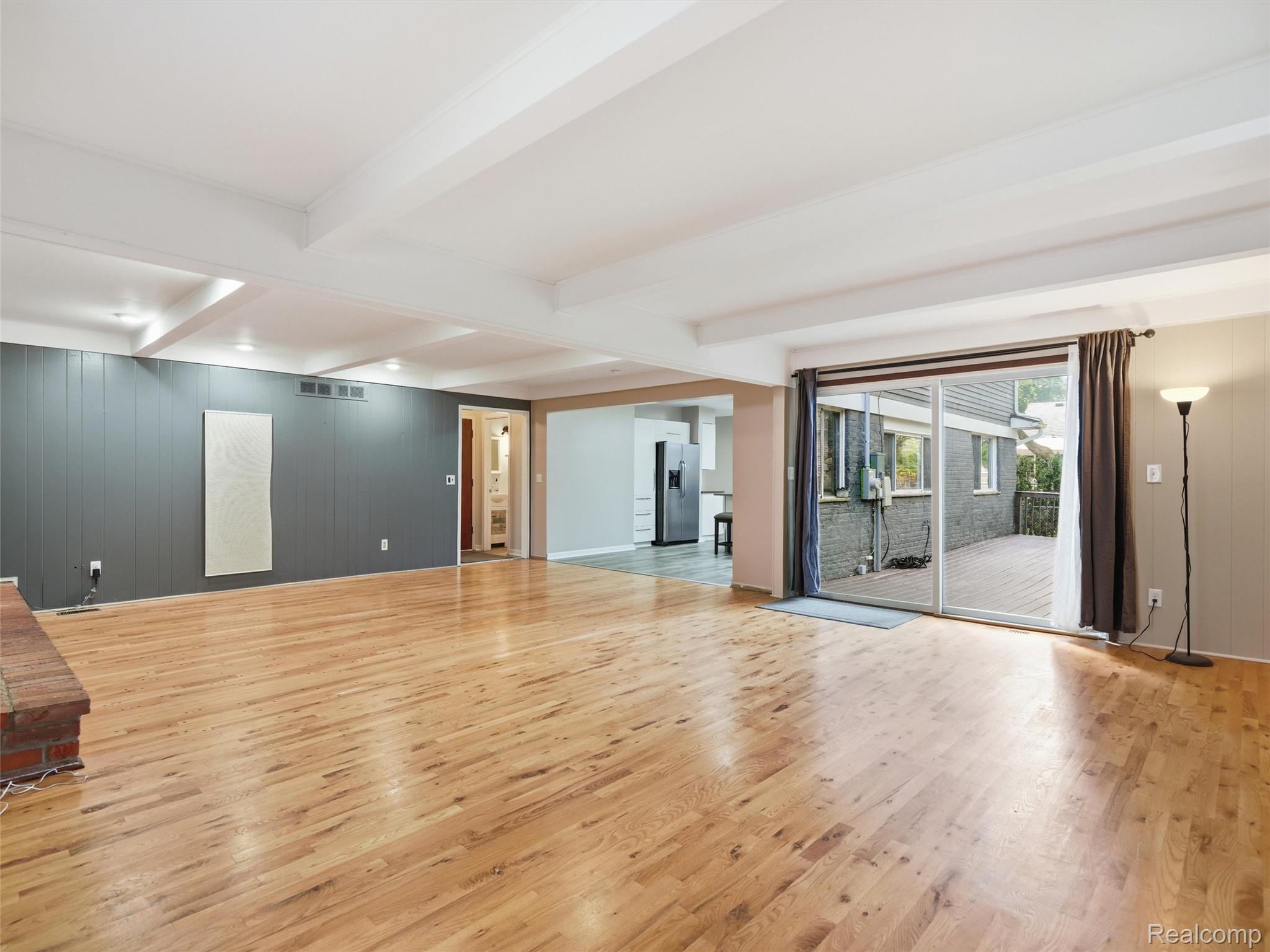 Open living room with hardwood floors, beamed ceiling, and sliding glass doors to a deck.
