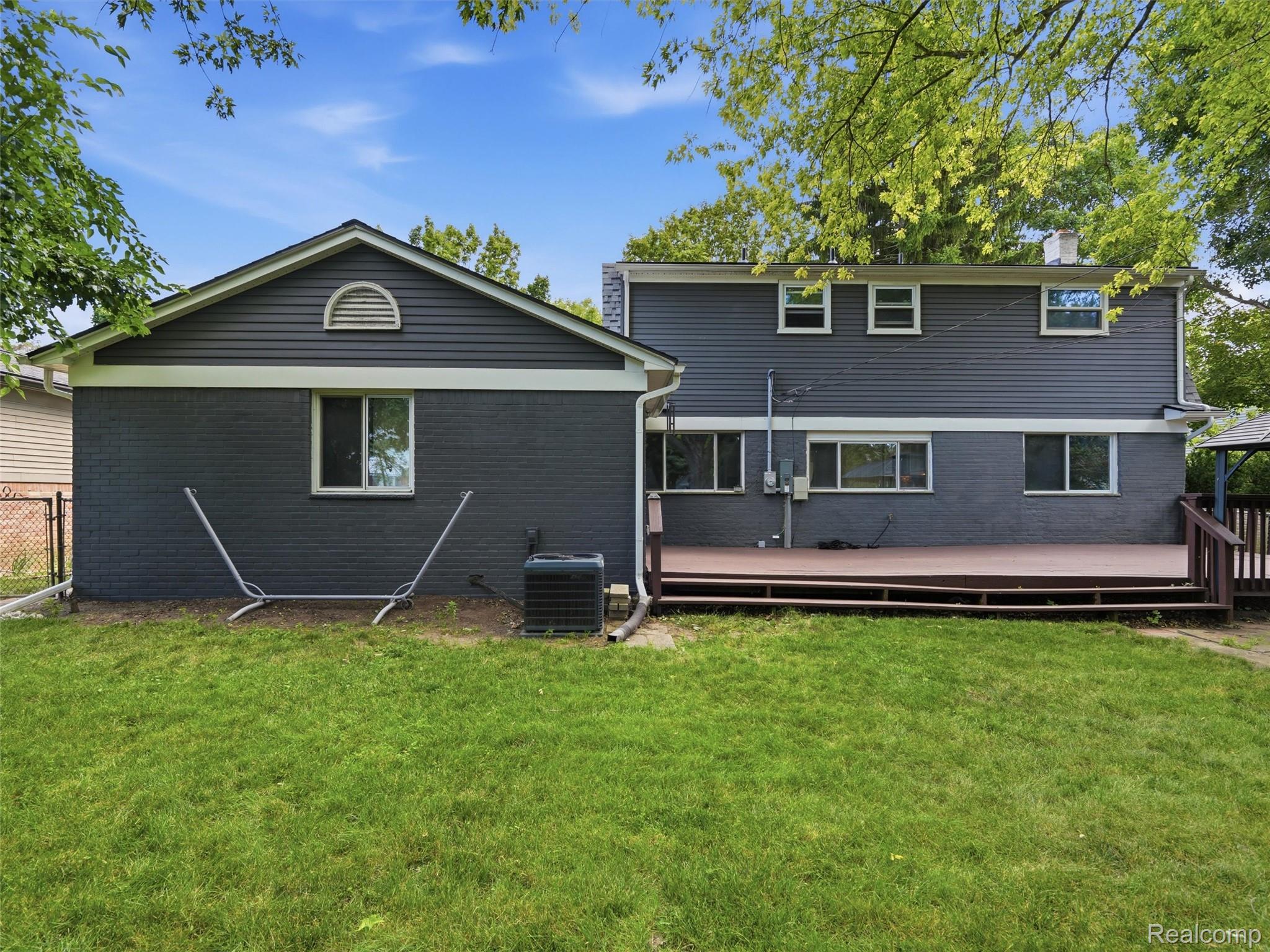 Rear of a dark gray house with a wooden deck and broad green lawn