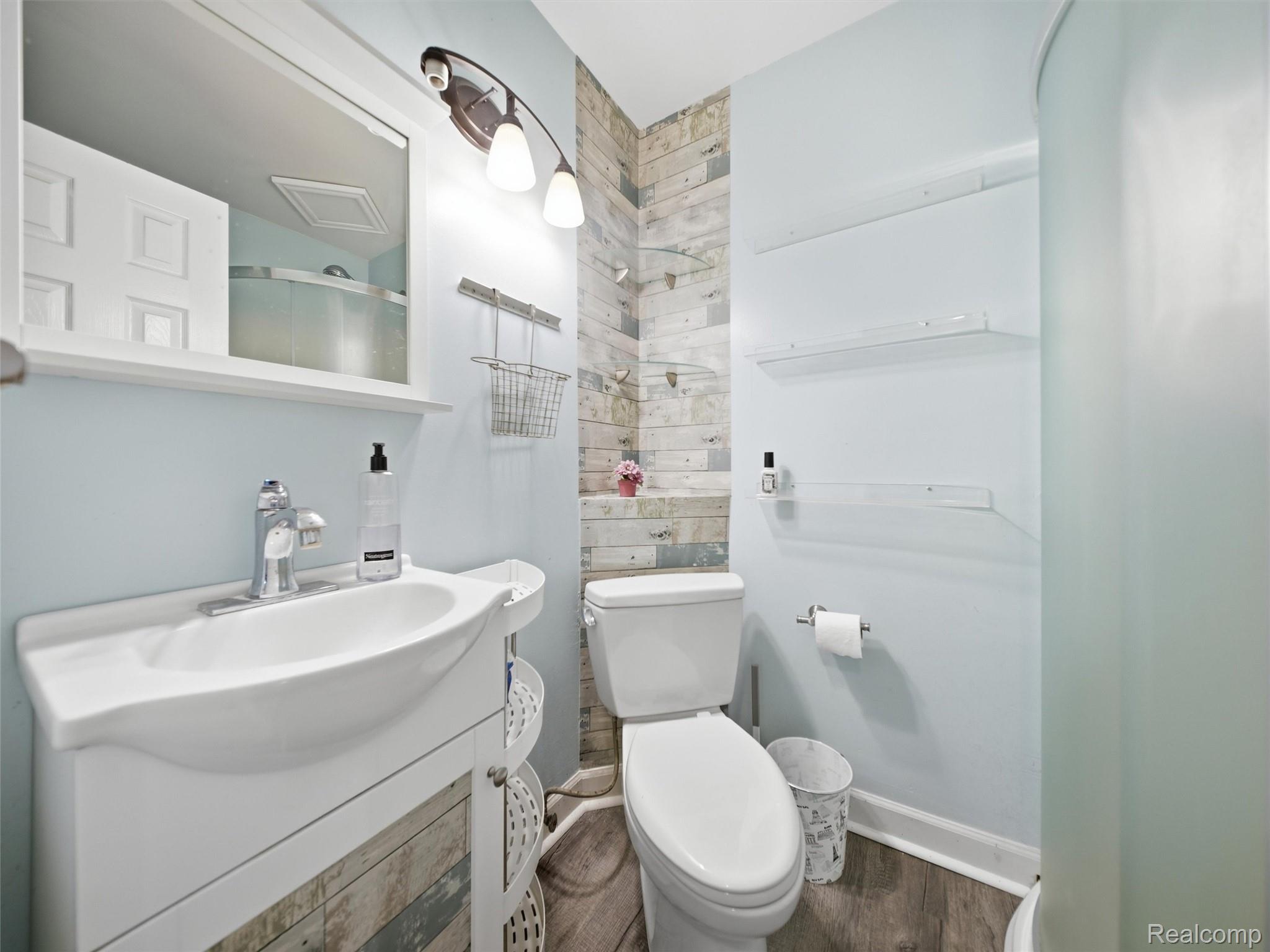 Bathroom with a white vanity, toilet, glass shower, and rustic wood-plank accent wall.