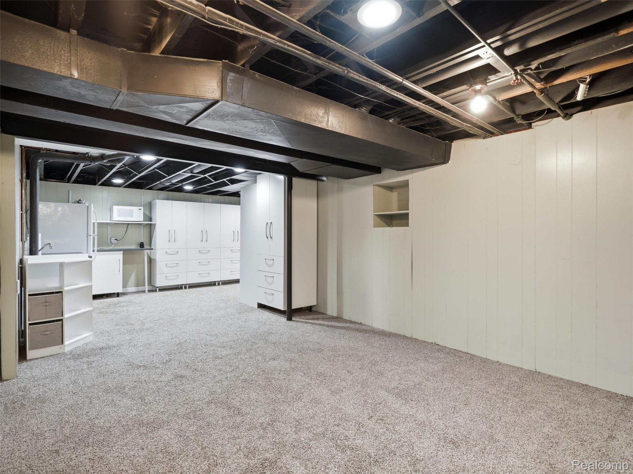 Basement with carpet, exposed ceiling ductwork, and built-in white storage cabinets.