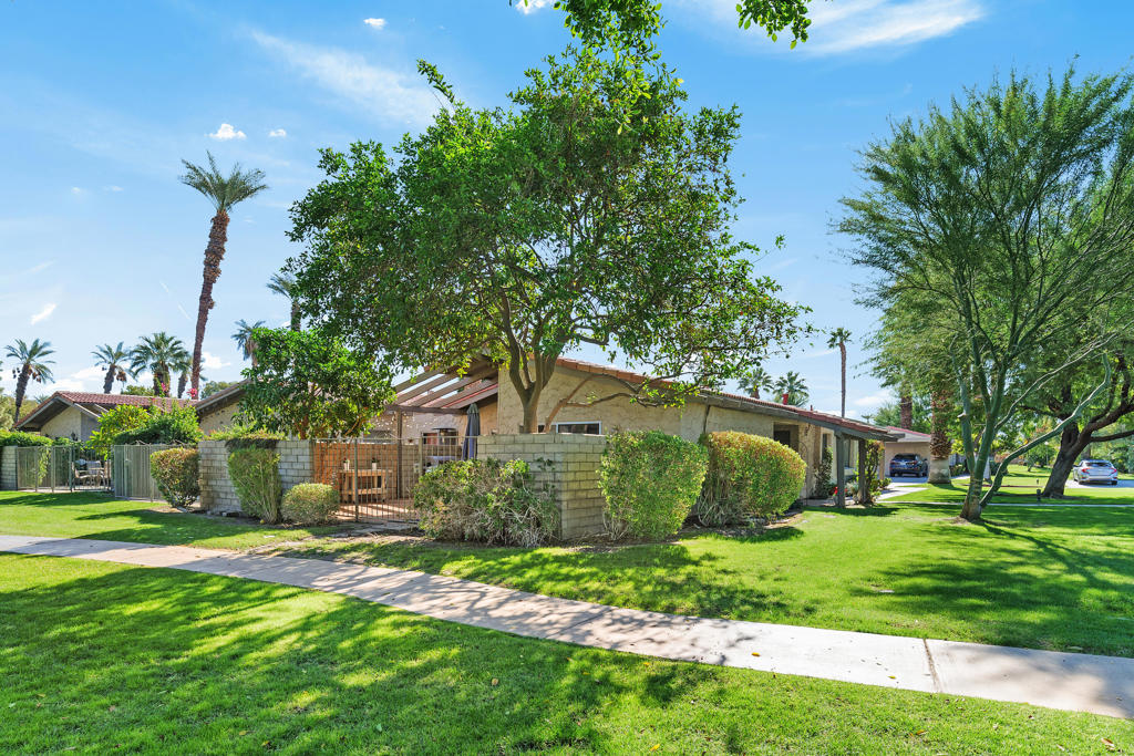 Single-story home with a covered patio, mature trees, and a broad green lawn.