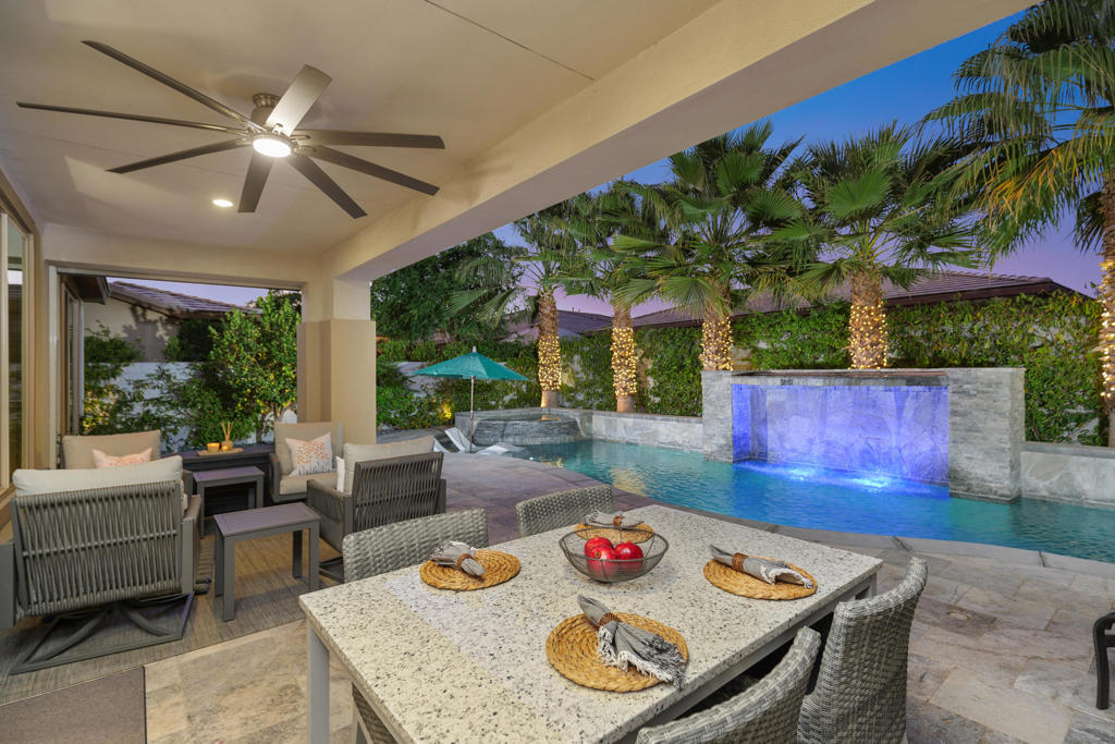 Covered patio with wicker furniture overlooks a pool with a blue-lit waterfall.
