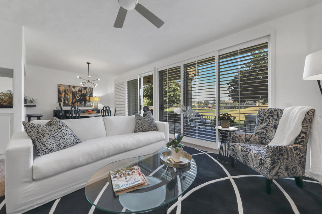 Bright living room with a white sofa and large windows overlooking a green lawn.