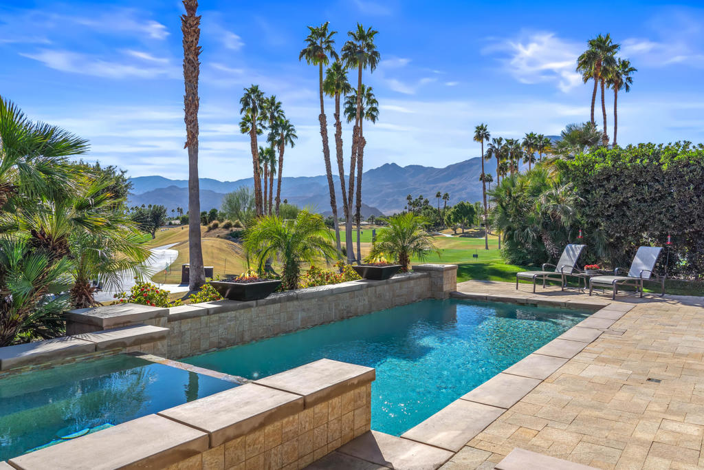 Pool patio overlooking a golf course, with palm trees and mountains beyond.
