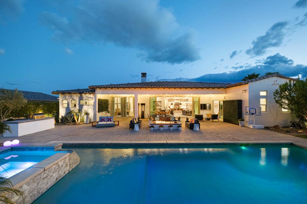 Back of a single-story home with a swimming pool and furnished patio at dusk.