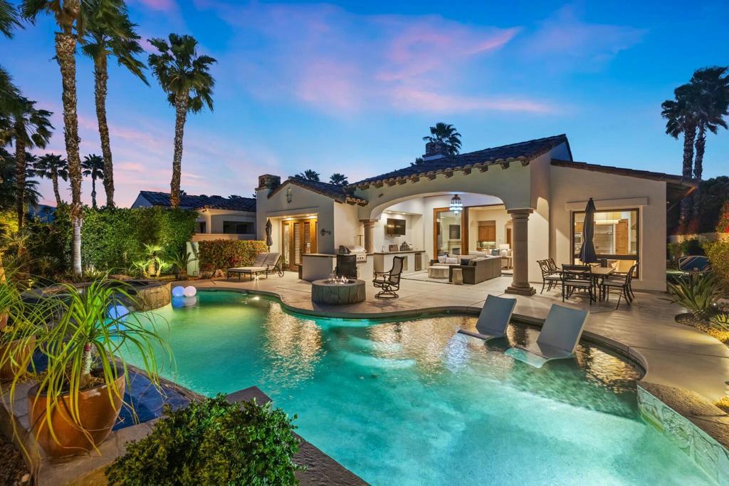 La Quinta home with a turquoise pool, in-water loungers, and covered outdoor living area at dusk.