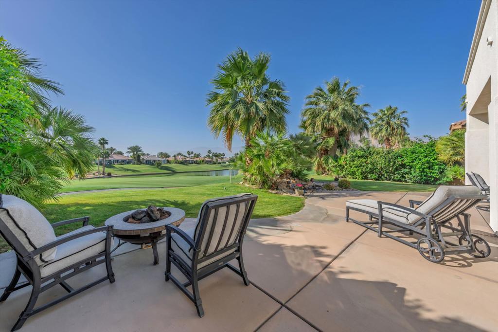 Furnished patio overlooking a golf course, with a fire pit, palm trees, and pond.