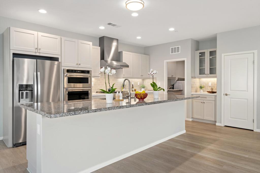 Modern kitchen with a large granite island, white cabinetry, stainless steel appliances, and orchids.