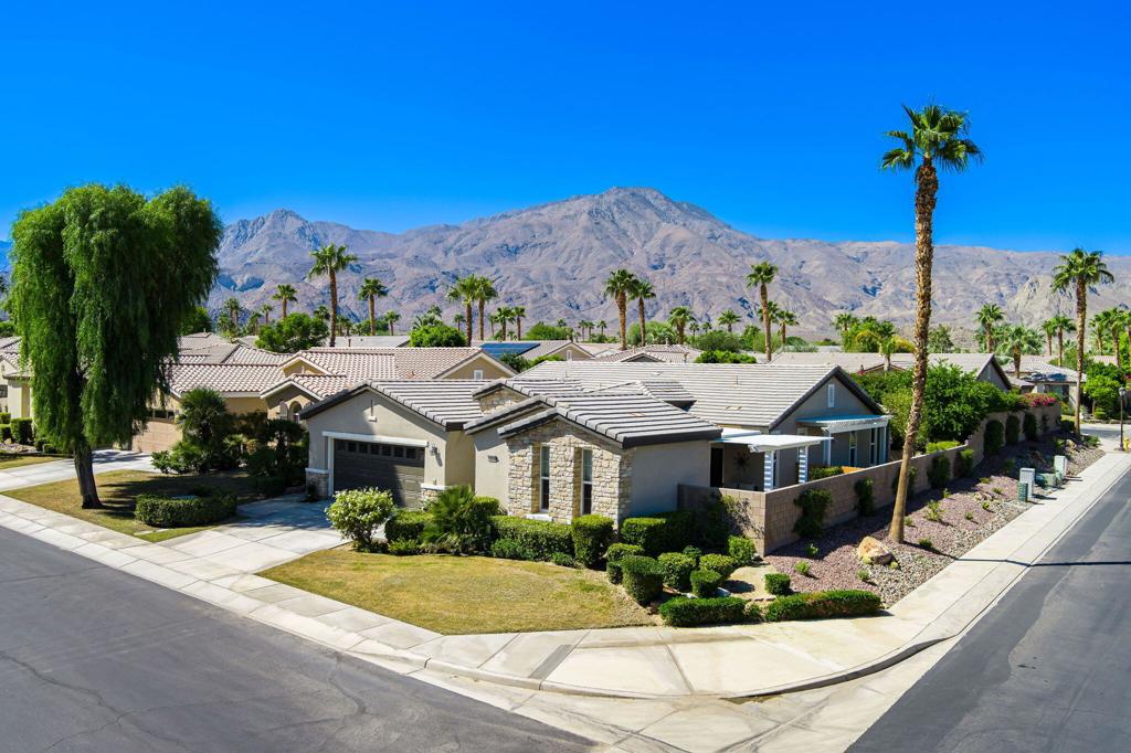Single-story stucco home on a landscaped corner lot, with palm trees and mountains in the background.