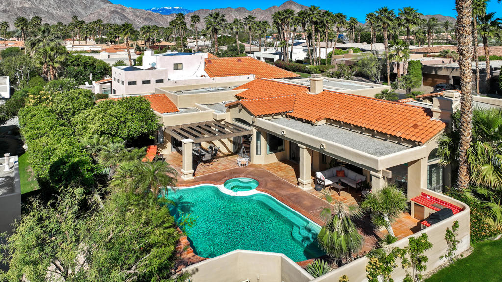 La Quinta home with a curved pool and spa, terracotta roofs, palm trees, and mountain views.