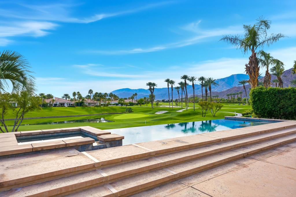 Swimming pool overlooking a palm-lined golf course, with mountains in the distance.