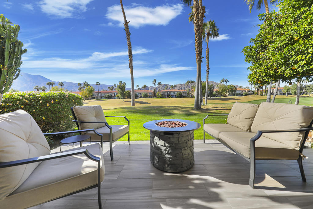 Furnished patio with a stone fire pit overlooking a golf course and distant mountains.