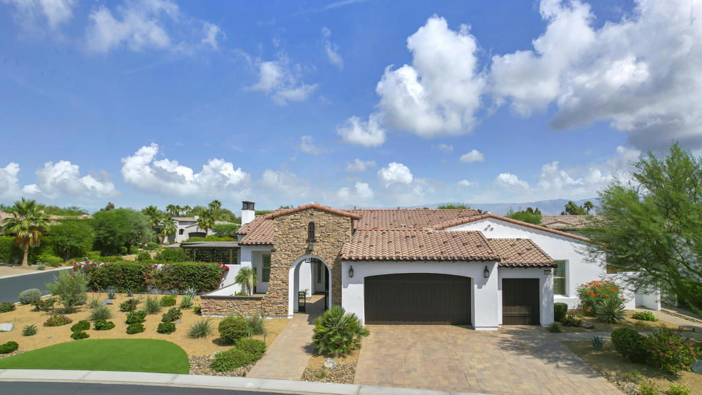 Home exterior with a stone arched entry, terracotta tile roof, and landscaped desert garden.