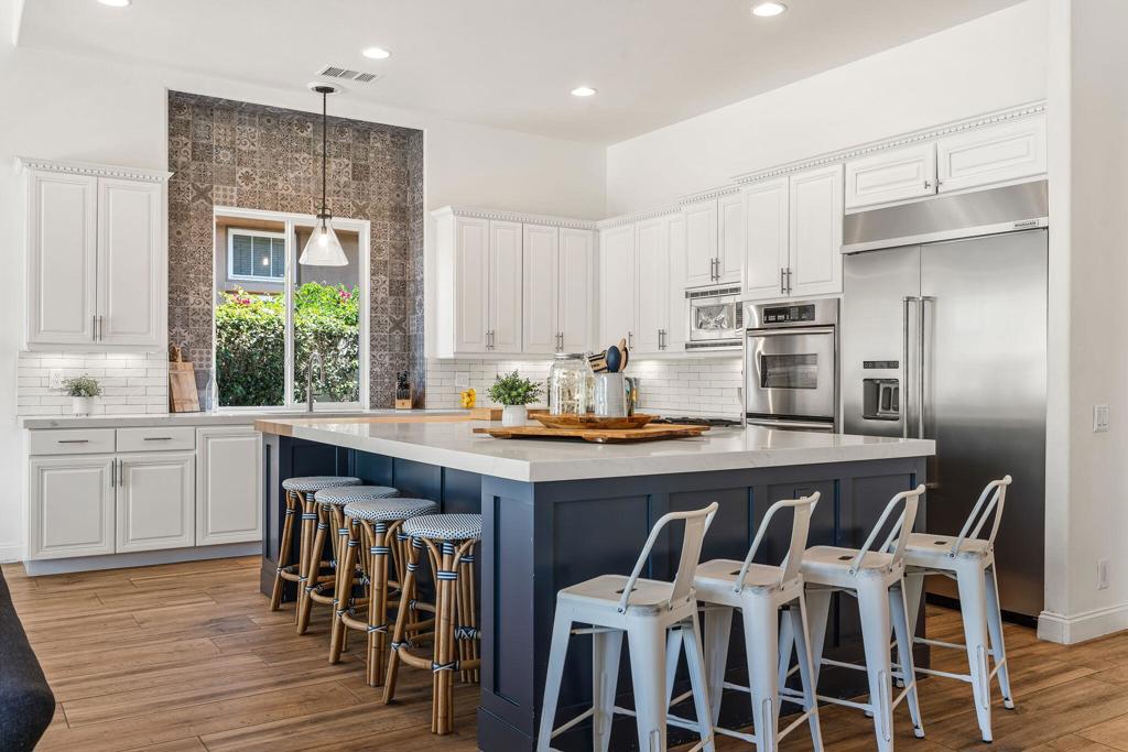Kitchen with a large navy island, white cabinets, stainless steel appliances, and patterned tile around the window.